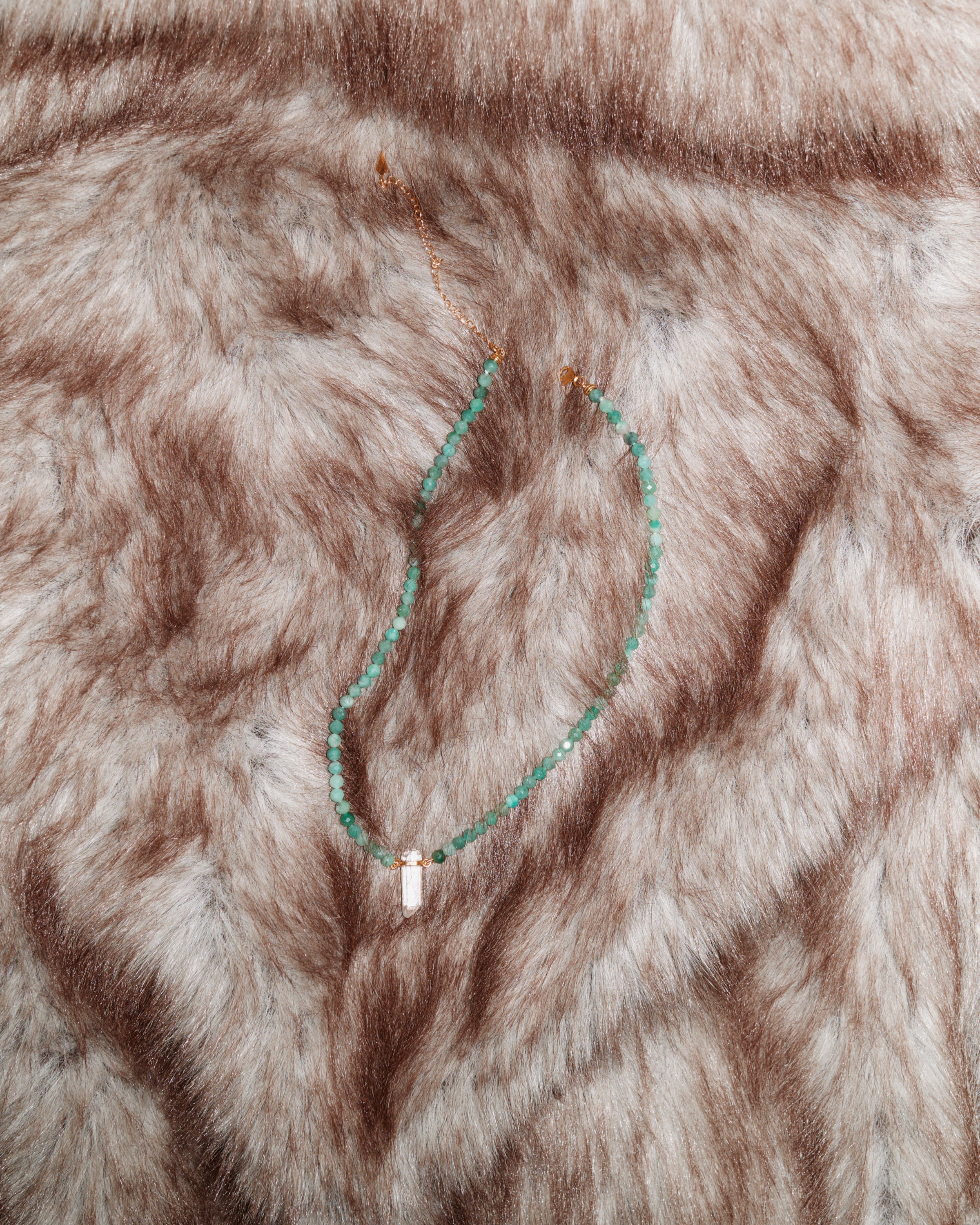 ENCARA VIRID Emerald necklace with raw polished quartz point pendant, gold 8 cm extension chain and clasp, arrowhead-shaped fantasy signature, and 4 mm faceted emerald bead strand.