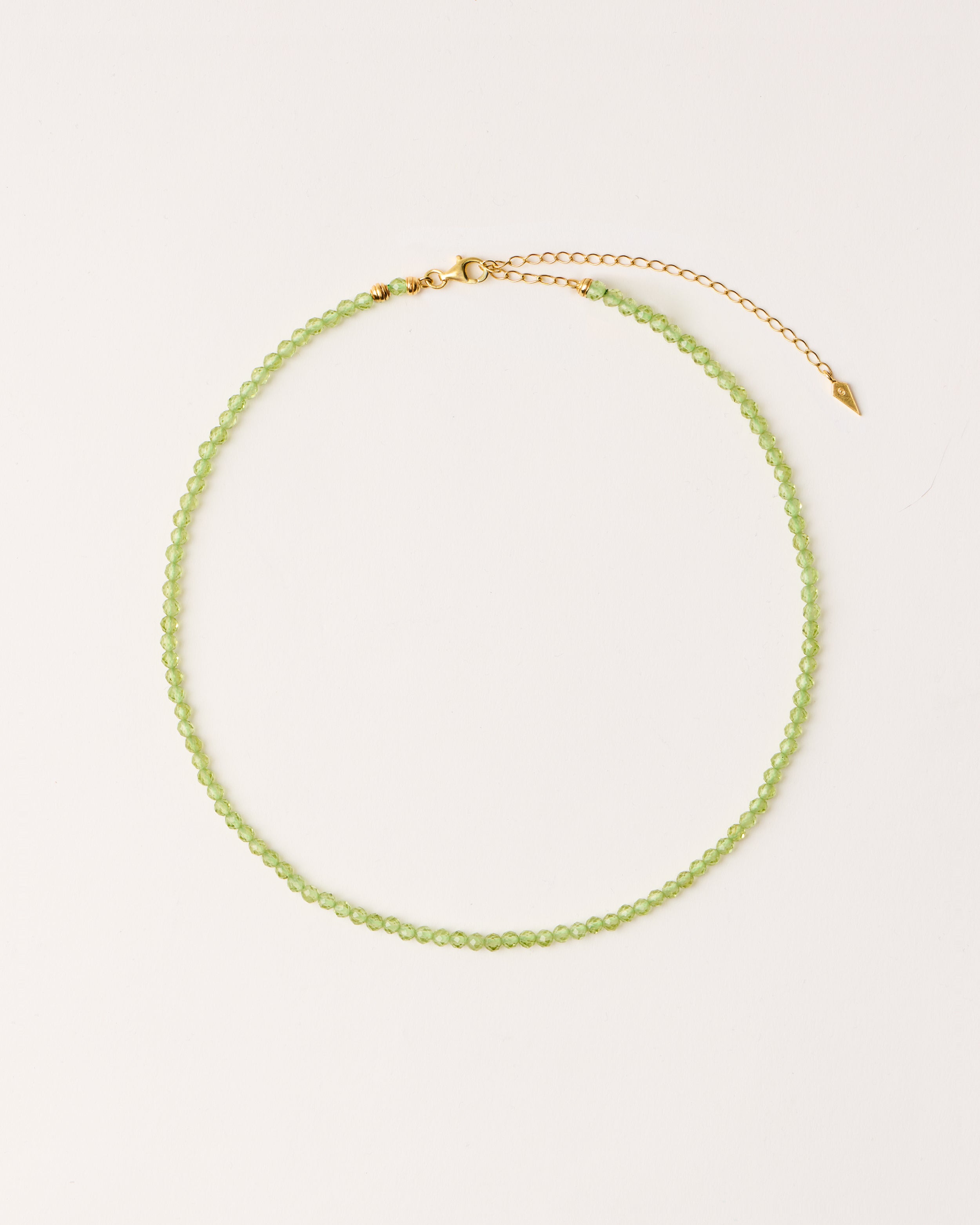 ETERNA OLMAR Peridot necklace with polished gold-plated silver spiral bead, 8 cm extension chain and clasp, arrowhead-shaped fantasy signature, and 4 mm faceted chrysolite bead strand.