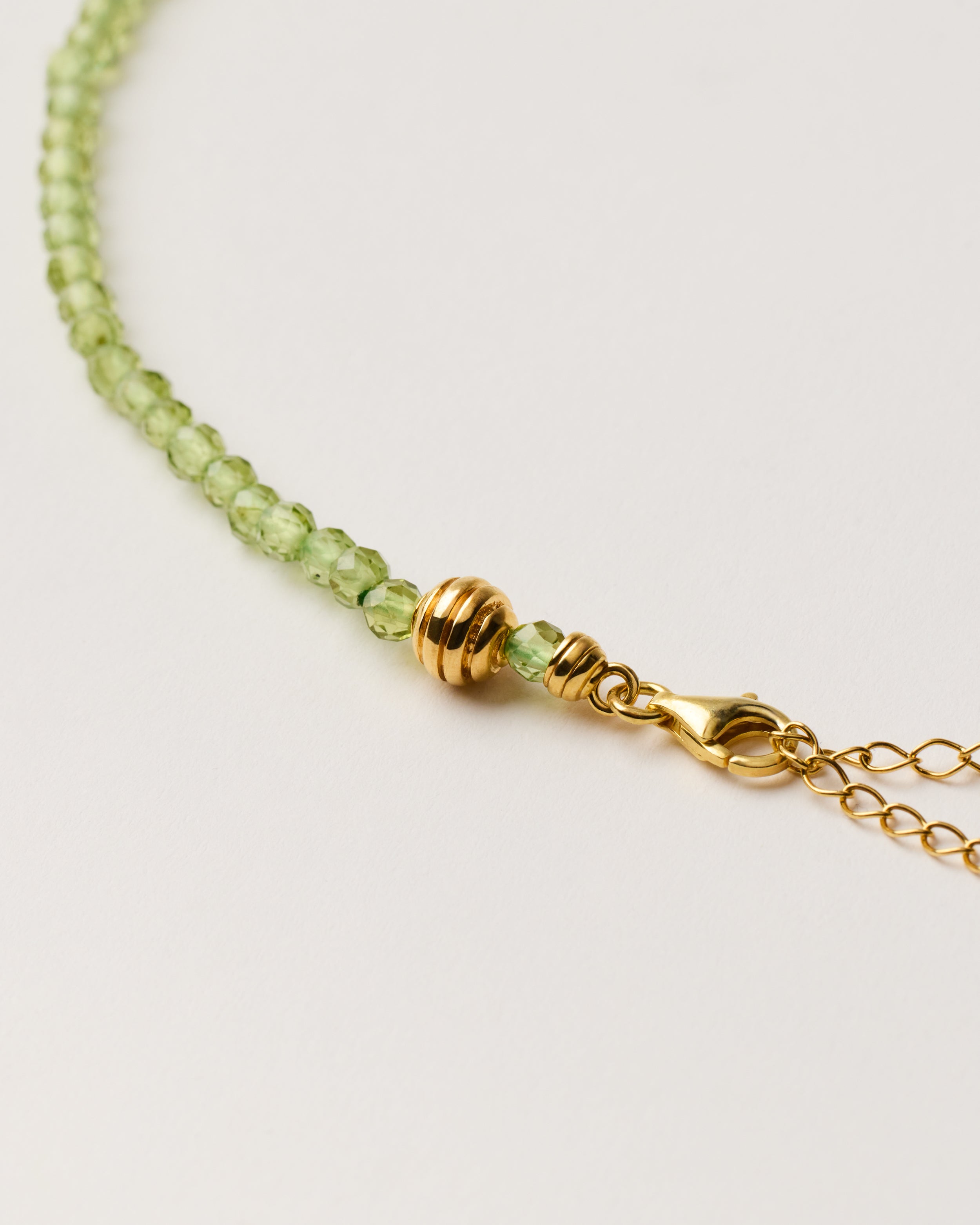 ETERNA OLMAR Peridot necklace with polished gold-plated silver spiral bead, 8 cm extension chain and clasp, arrowhead-shaped fantasy signature, and 4 mm faceted chrysolite bead strand.