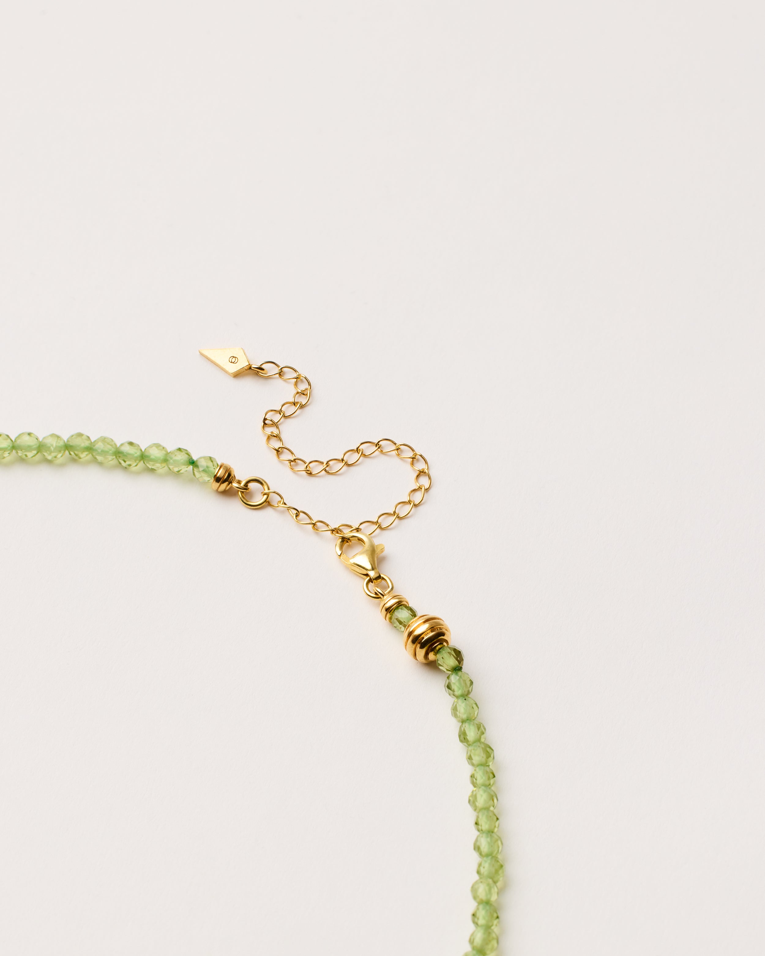ETERNA OLMAR Peridot necklace with polished gold-plated silver spiral bead, 8 cm extension chain and clasp, arrowhead-shaped fantasy signature, and 4 mm faceted chrysolite bead strand.