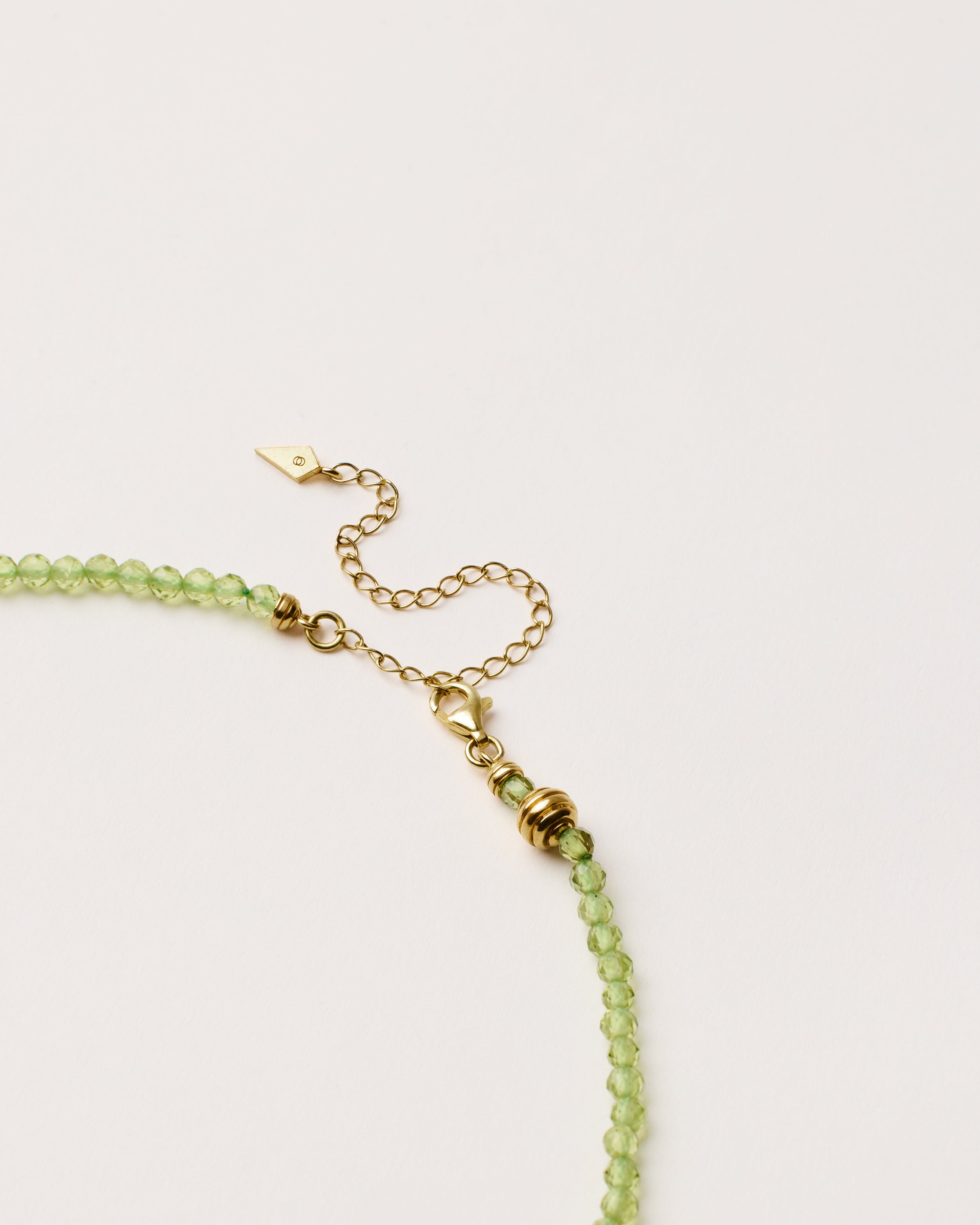 ETERNA OLMAR Peridot necklace with polished gold spiral bead, 8 cm extension chain and clasp, arrowhead-shaped fantasy signature, and 4 mm faceted chrysolite bead strand.