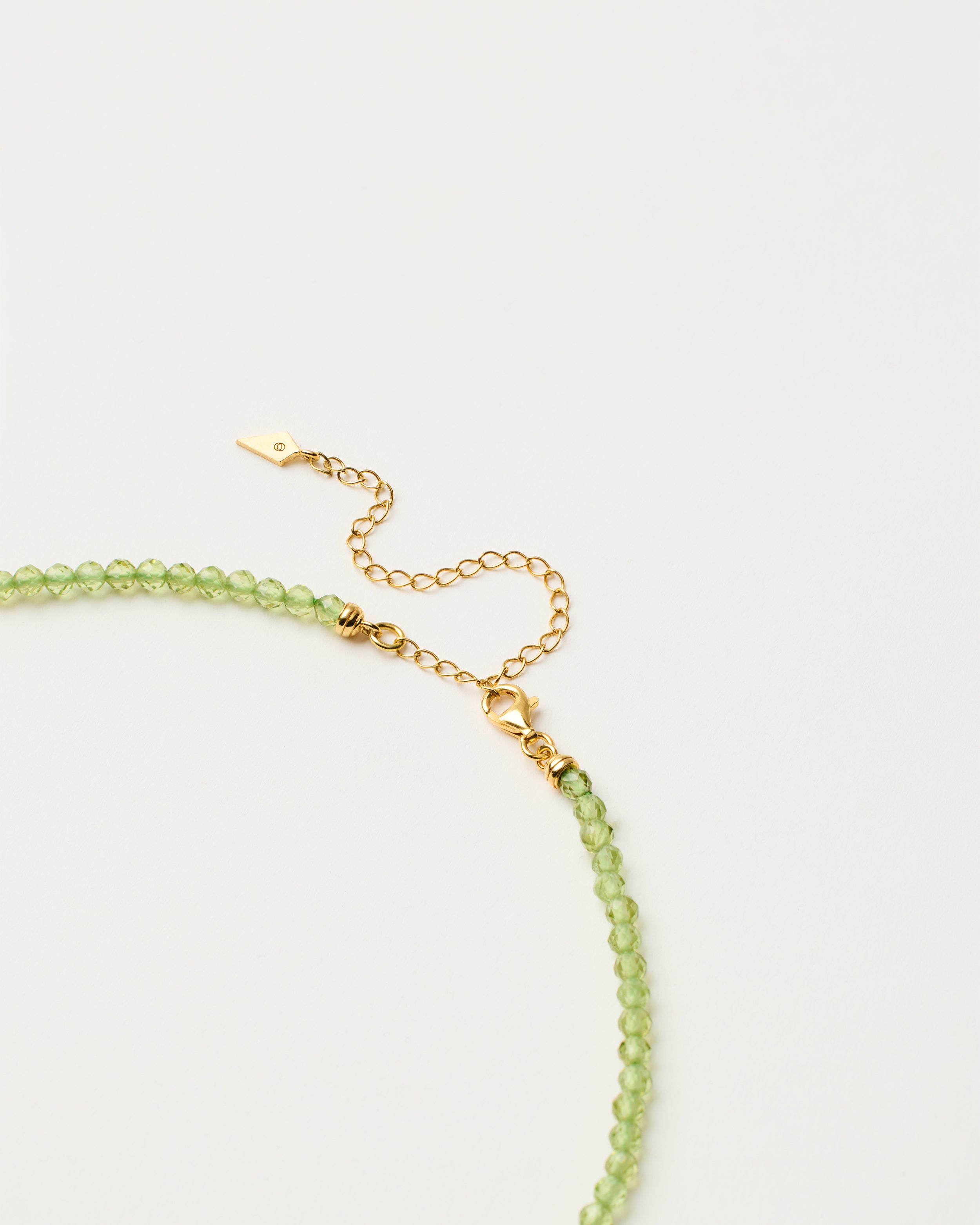 ENCARA OLMAR Peridot necklace with raw polished quartz point pendant, gold-plated silver 8 cm extension chain and clasp, arrowhead-shaped fantasy signature, and 4 mm faceted chrysolite bead strand.