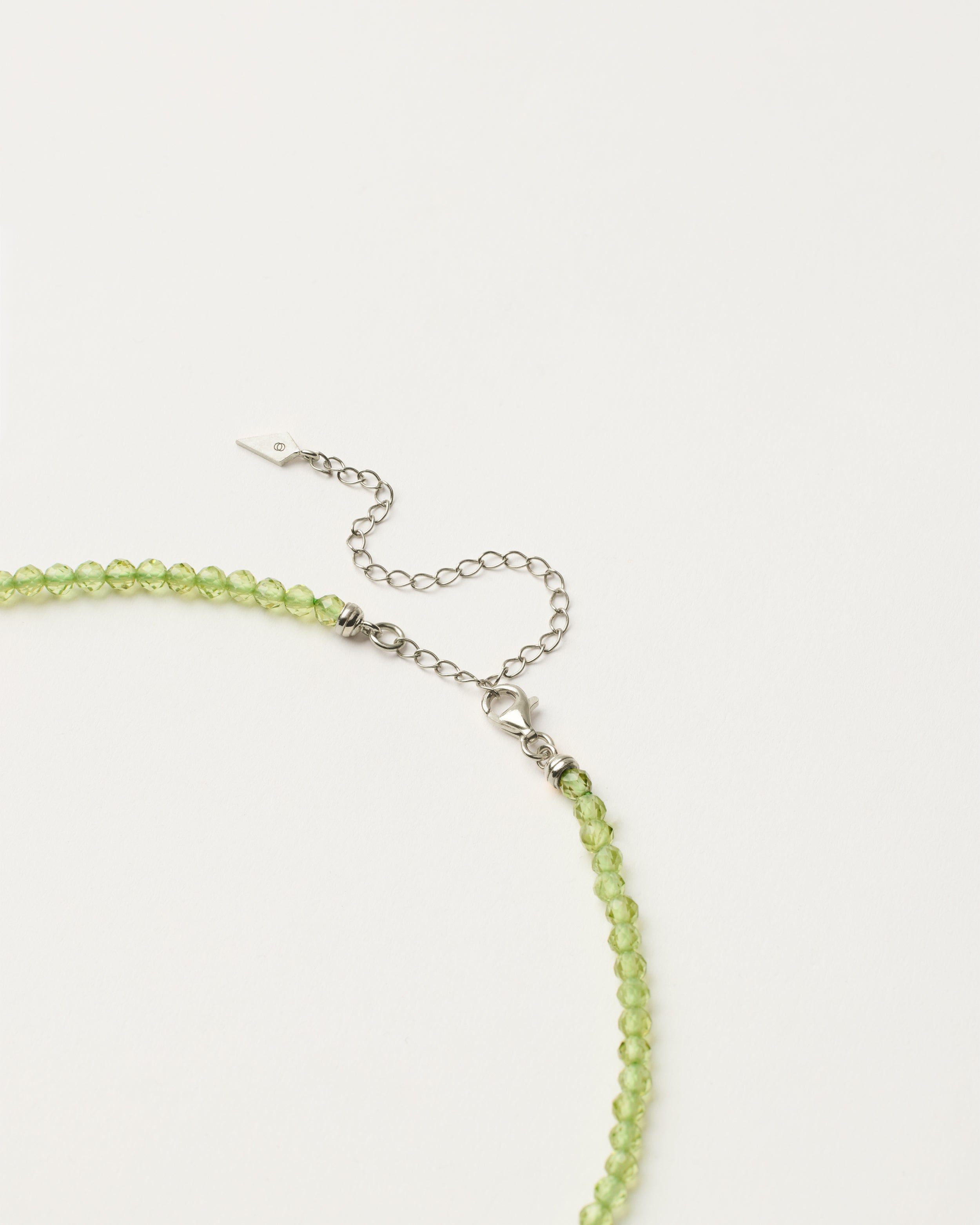 ENCARA OLMAR Peridot necklace with raw polished quartz point pendant, silver 8 cm extension chain and clasp, arrowhead-shaped fantasy signature, and 4 mm faceted chrysolite bead strand.