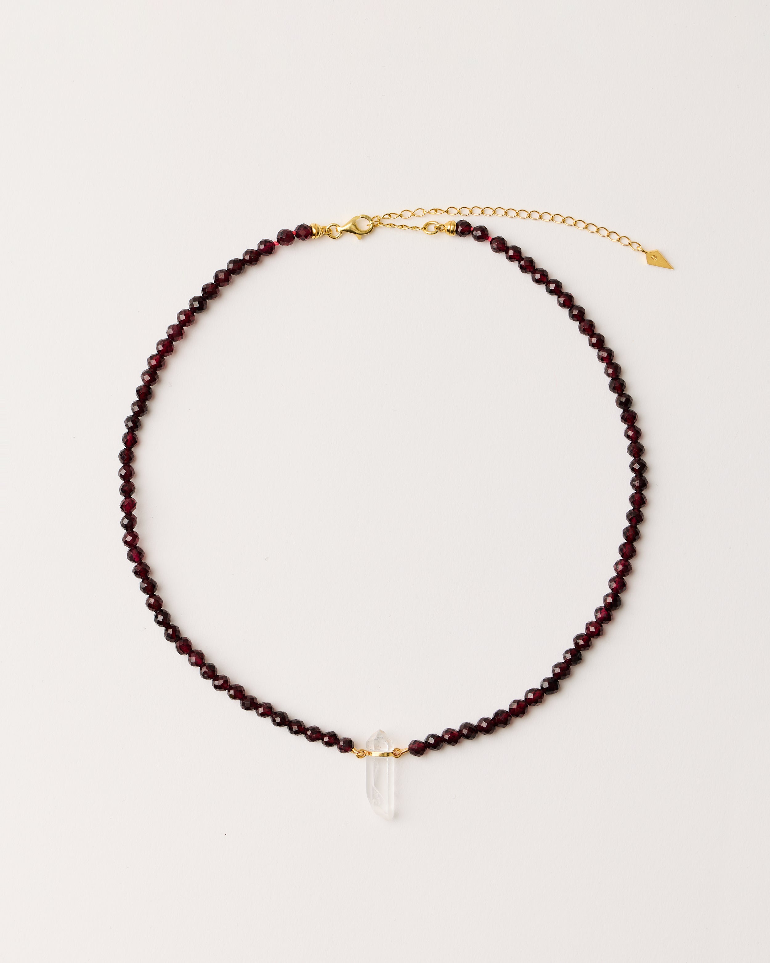 ENCARA INFERA Garnet necklace with raw polished quartz point pendant, gold-plated silver 8 cm extension chain and clasp, arrowhead-shaped fantasy signature, and 4 mm faceted garnet bead strand.