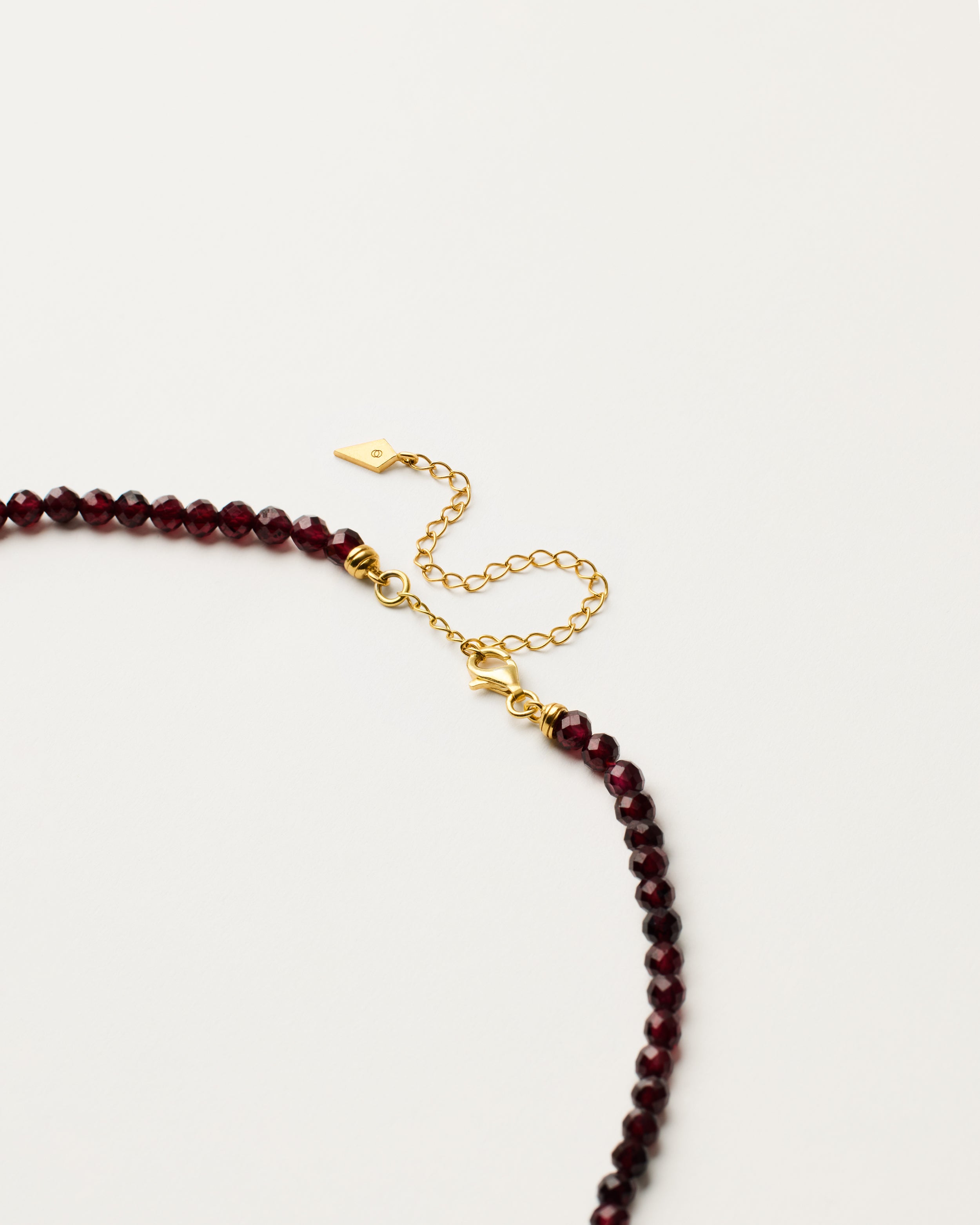 ENCARA INFERA Garnet necklace with raw polished quartz point pendant, gold-plated silver 8 cm extension chain and clasp, arrowhead-shaped fantasy signature, and 4 mm faceted garnet bead strand.