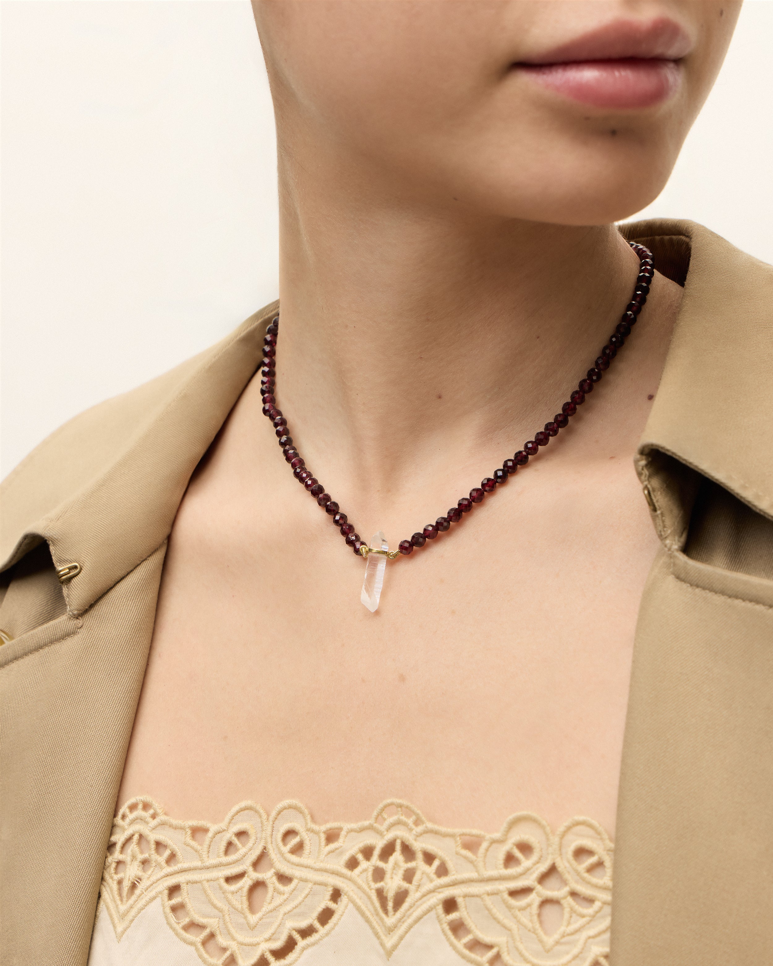 ENCARA INFERA Garnet necklace with raw polished quartz point pendant, gold 8 cm extension chain and clasp, arrowhead-shaped fantasy signature, and 4 mm faceted garnet bead strand.