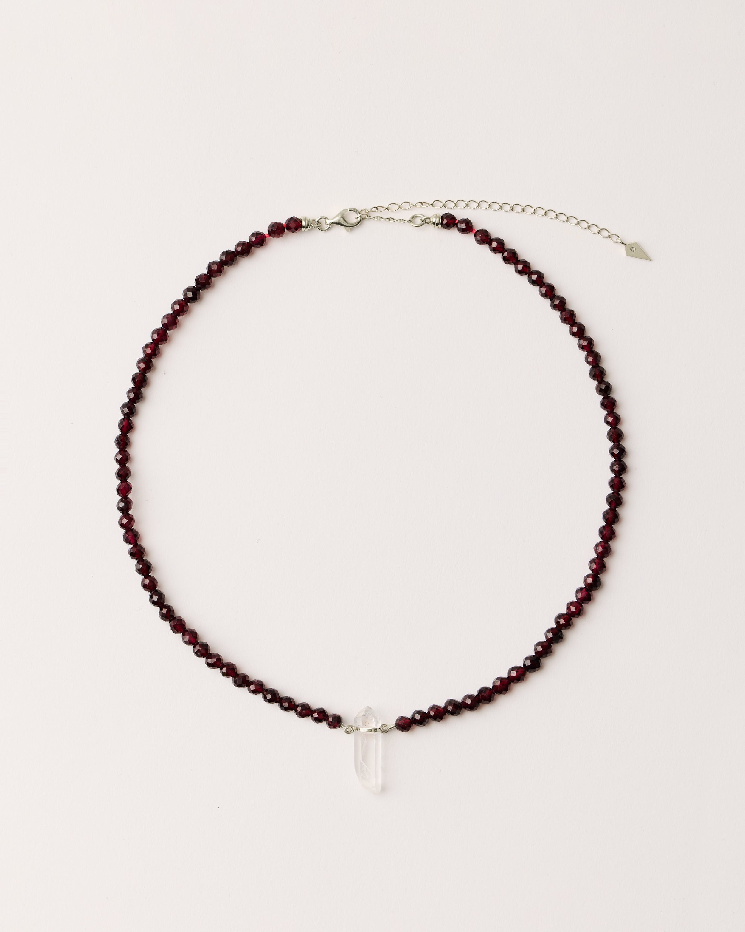 ENCARA INFERA Garnet necklace with raw polished quartz point pendant, silver 8 cm extension chain and clasp, arrowhead-shaped fantasy signature, and 4 mm faceted garnet bead strand.