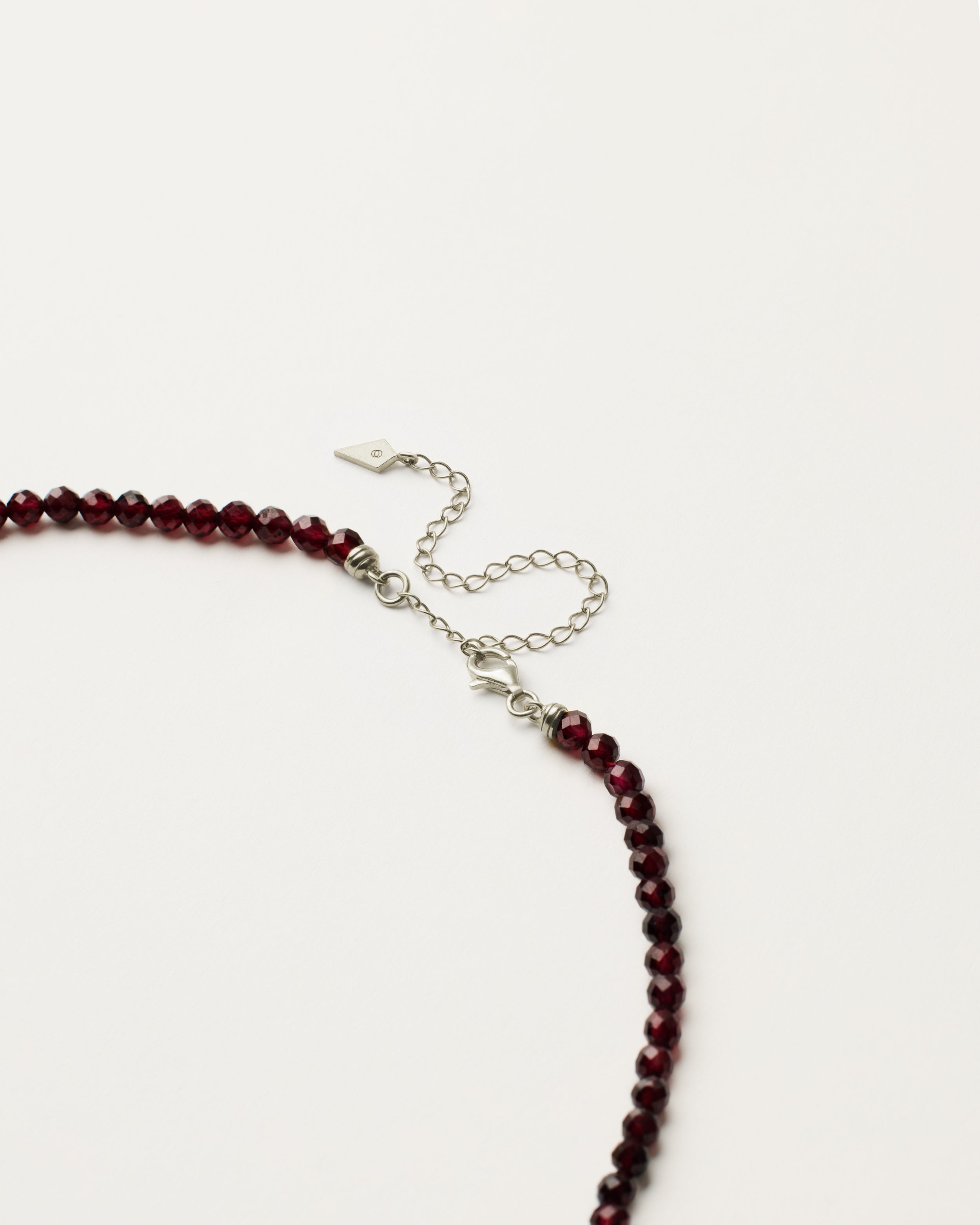 ENCARA INFERA Garnet necklace with raw polished quartz point pendant, silver 8 cm extension chain and clasp, arrowhead-shaped fantasy signature, and 4 mm faceted garnet bead strand.