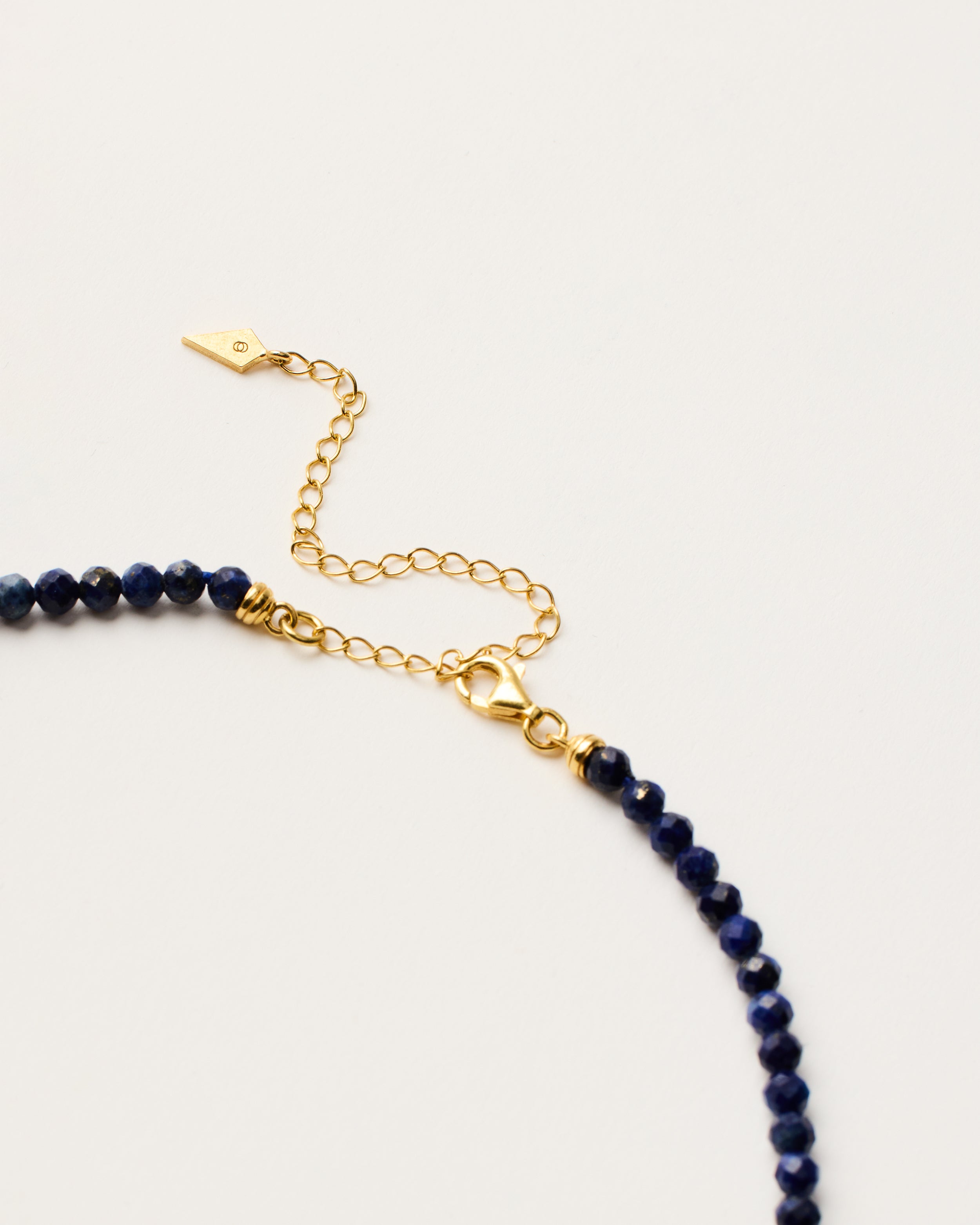 ENCARA NOCTA Lapis Lazuli necklace with raw polished quartz point pendant, gold-plated silver 8 cm extension chain and clasp, arrowhead-shaped fantasy signature, and 4 mm faceted lazurite bead strand.