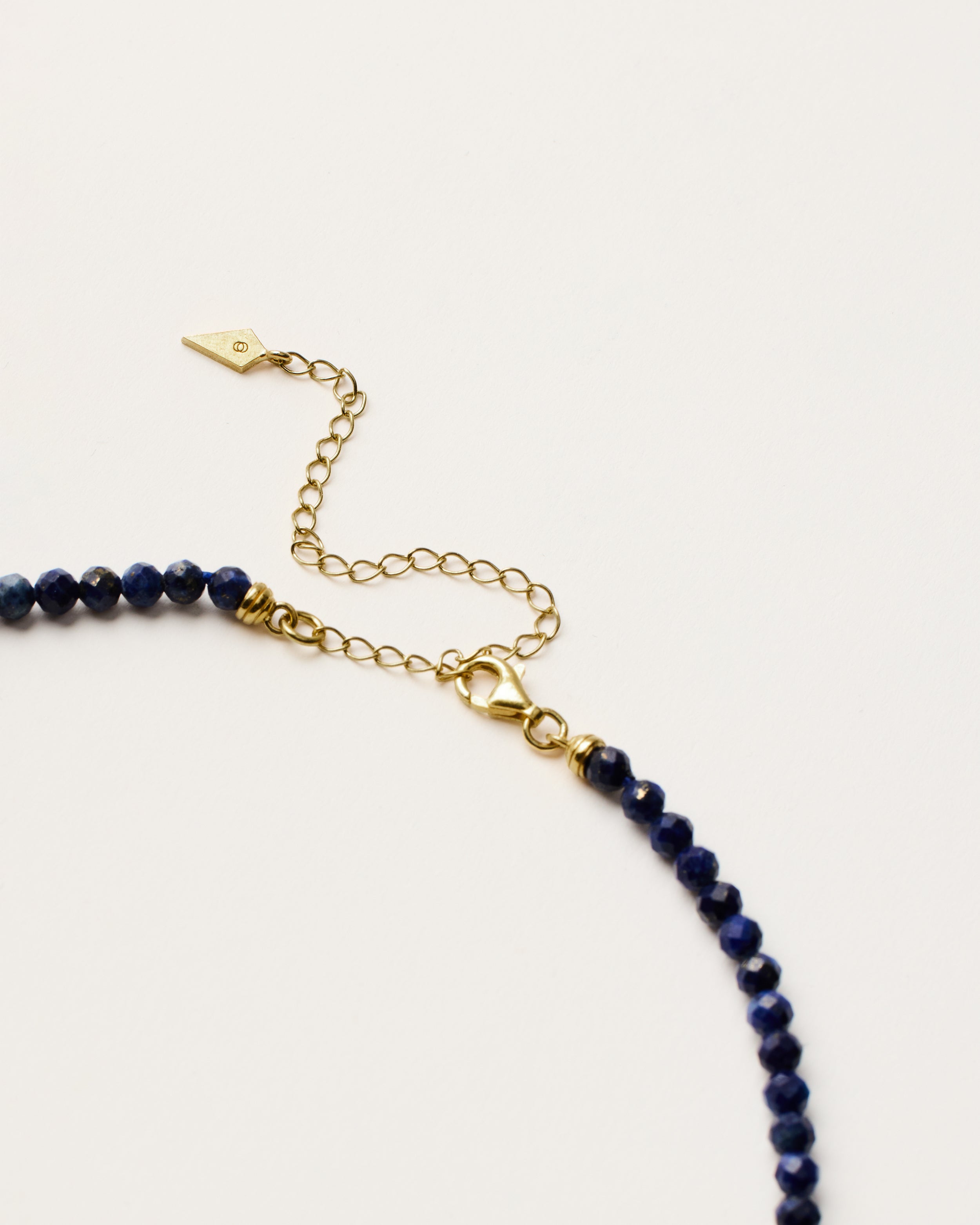 ENCARA NOCTA Lapis Lazuli necklace with raw polished quartz point pendant, gold 8 cm extension chain and clasp, arrowhead-shaped fantasy signature, and 4 mm faceted lazurite bead strand.