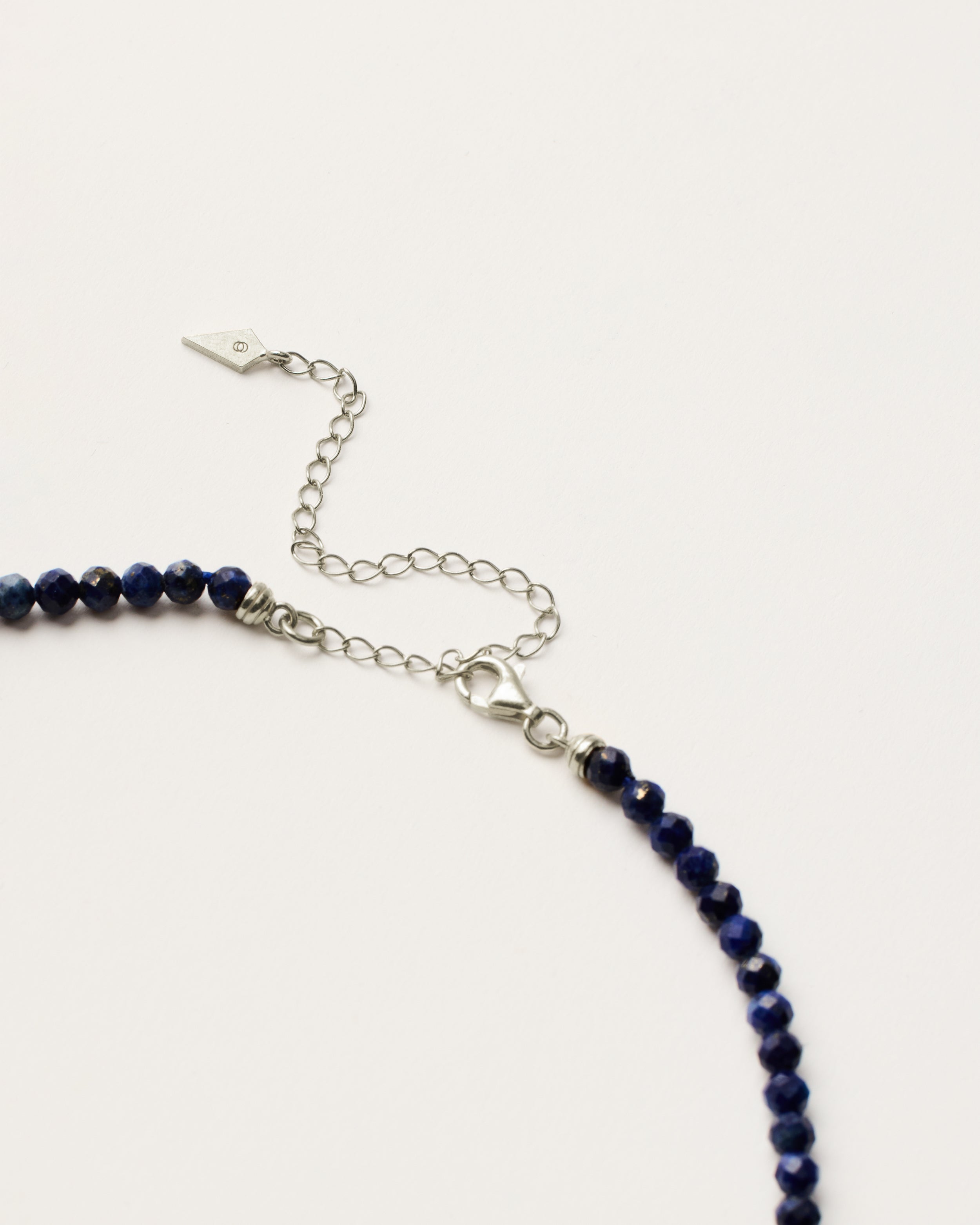 ENCARA NOCTA Lapis Lazuli necklace with raw polished quartz point pendant, silver 8 cm extension chain and clasp, arrowhead-shaped fantasy signature, and 4 mm faceted lazurite bead strand.