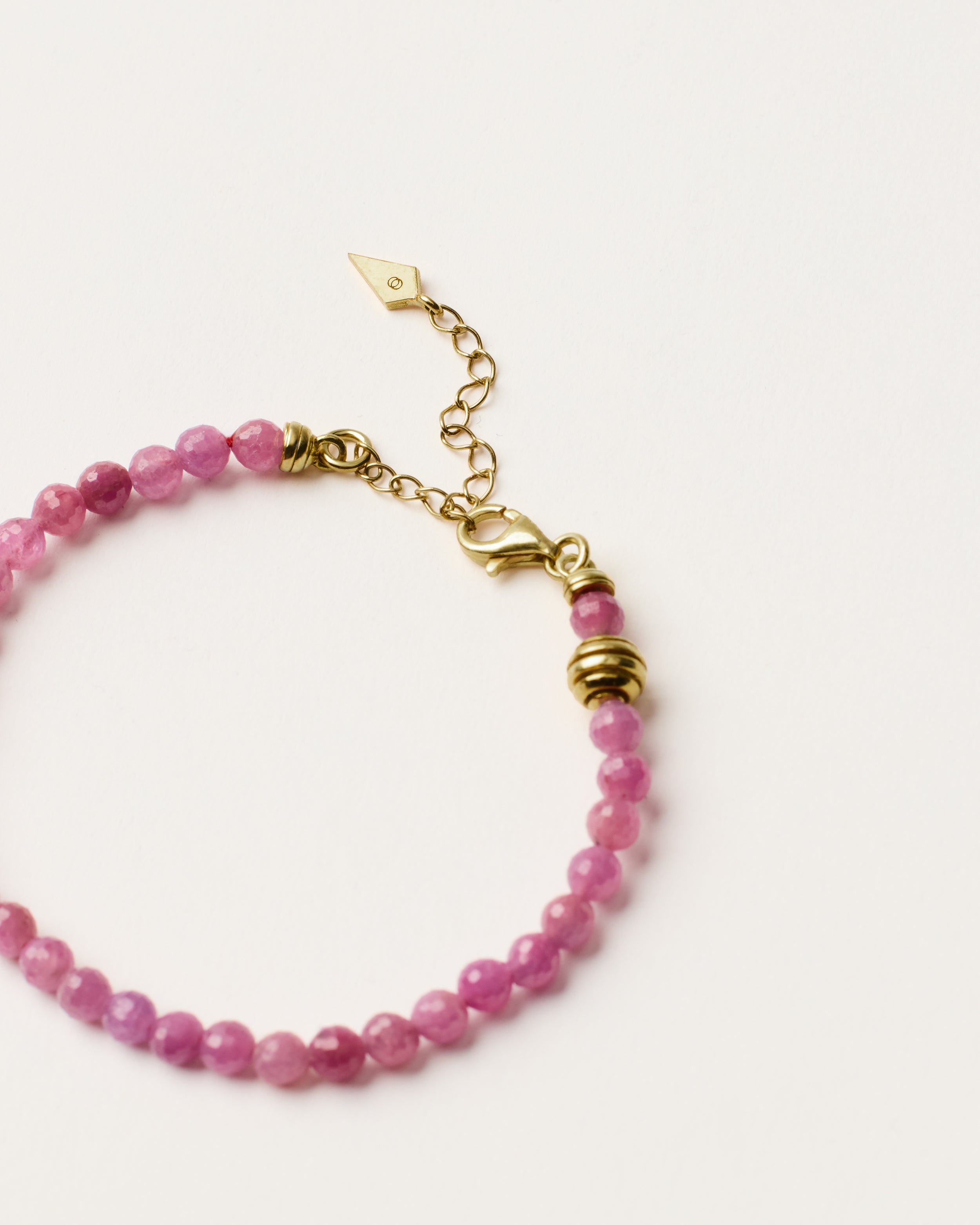 ETERNA CARMES Ruby bracelet with polished gold spiral bead, 4 cm extension chain and clasp, arrowhead-shaped fantasy signature, and 4 mm faceted ruby bead strand.