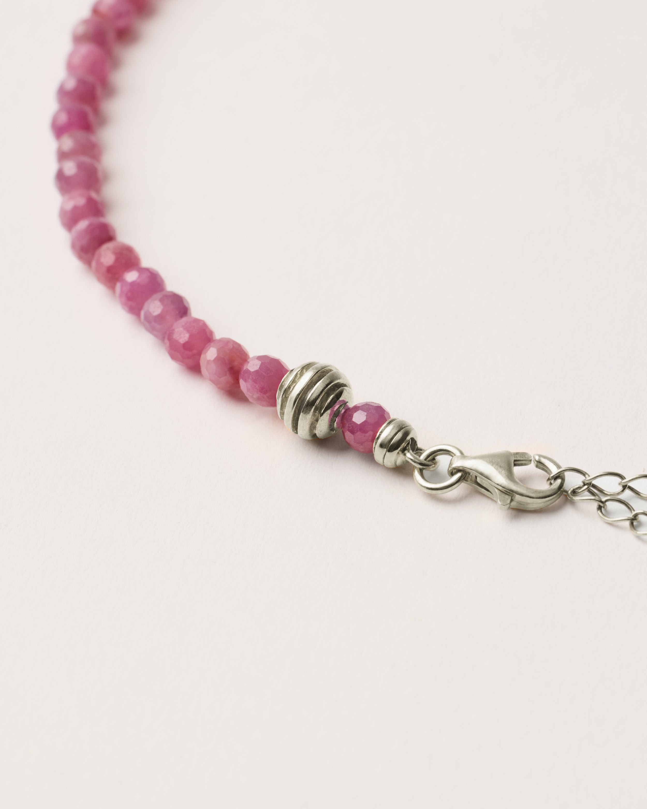ETERNA CARMES Ruby necklace with polished silver spiral bead, 8 cm extension chain and clasp, arrowhead-shaped fantasy signature, and 4 mm faceted ruby bead strand.