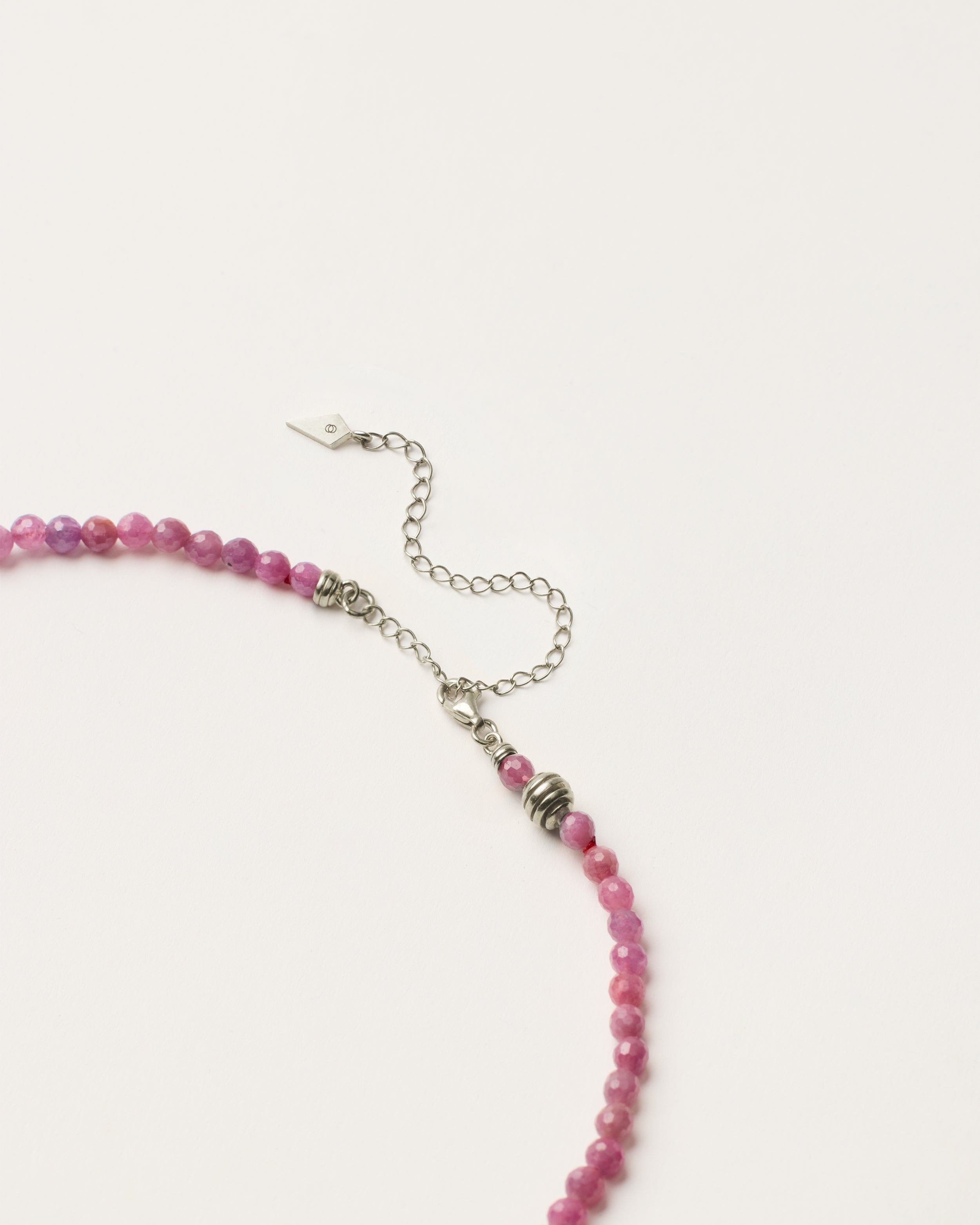 ETERNA CARMES Ruby necklace with polished silver spiral bead, 8 cm extension chain and clasp, arrowhead-shaped fantasy signature, and 4 mm faceted ruby bead strand.
