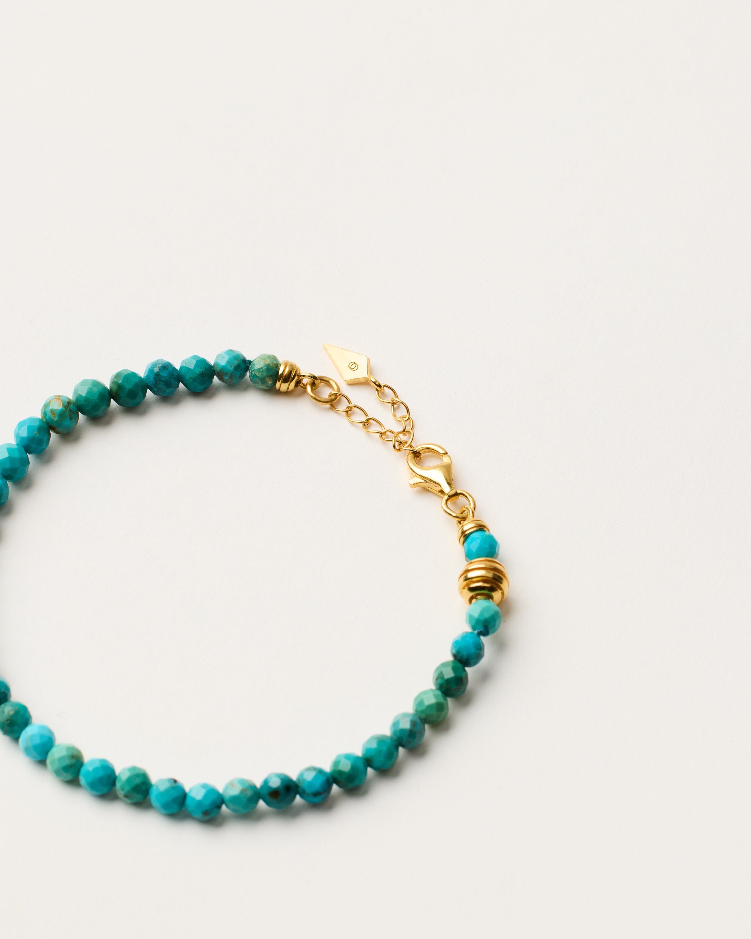 ETERNA AZURA Turquoise bracelet with polished gold-plated silver spiral bead, 4 cm extension chain and clasp, arrowhead-shaped fantasy signature, and 4 mm faceted turquoise bead strand.