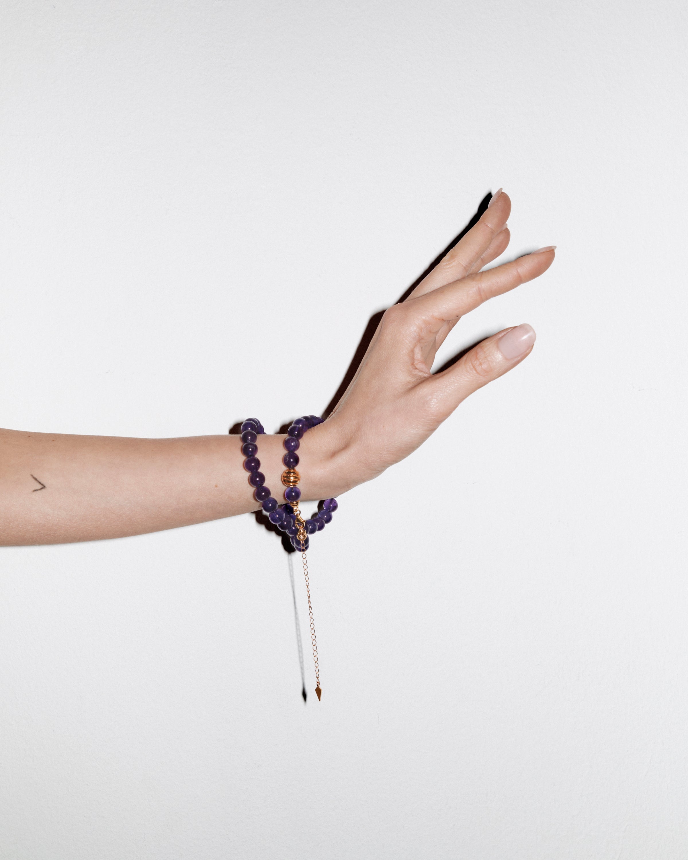 ETERNA VÉLA Amethyst necklace with polished gold spiral bead, 8 cm extension chain and clasp, arrowhead-shaped fantasy signature, and 8 mm faceted amethyst bead strand.