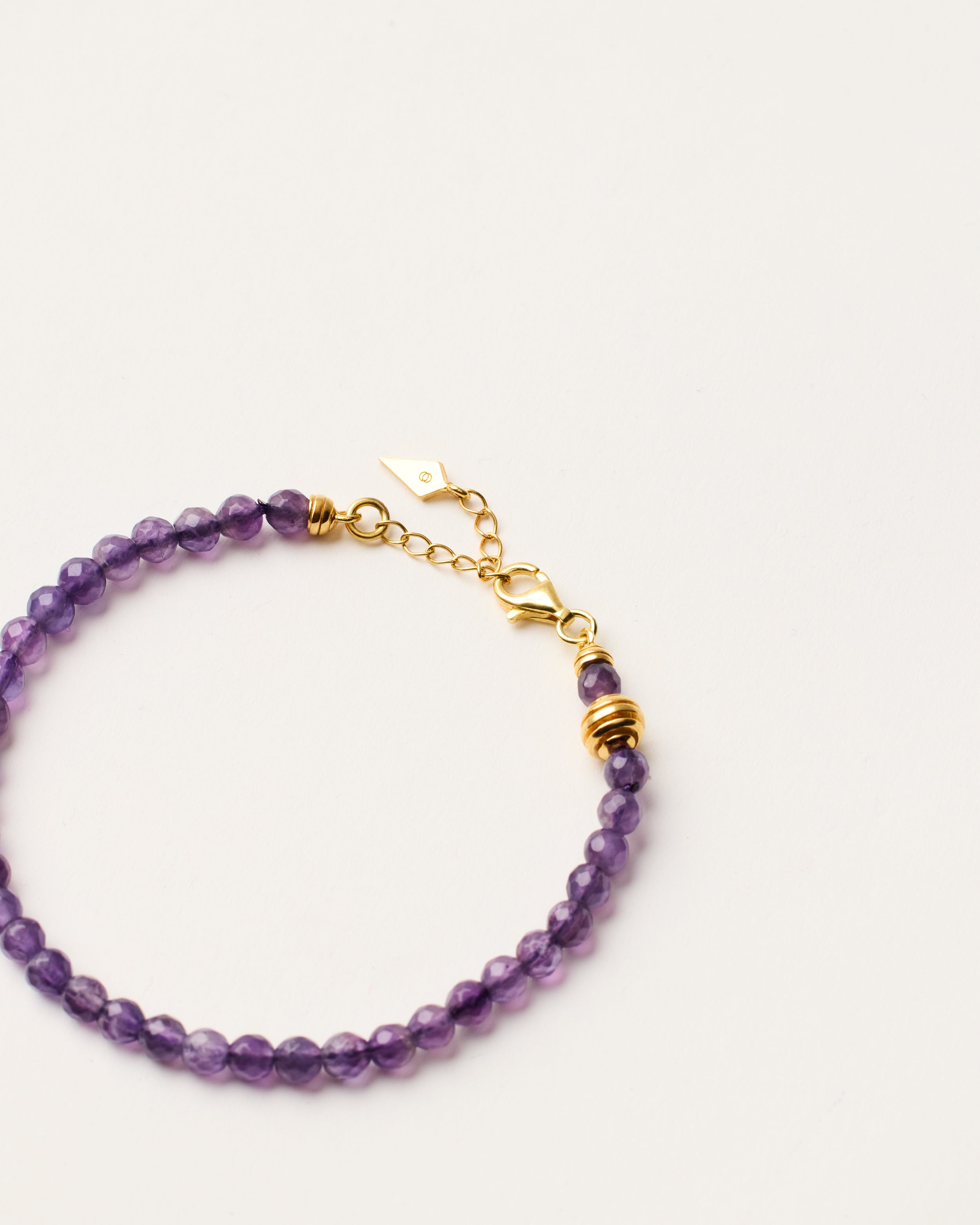 ETERNA VÉLA Amethyst bracelet with polished gold-plated silver spiral bead, 4 cm extension chain and clasp, arrowhead-shaped fantasy signature, and 4 mm faceted amethyst bead strand.