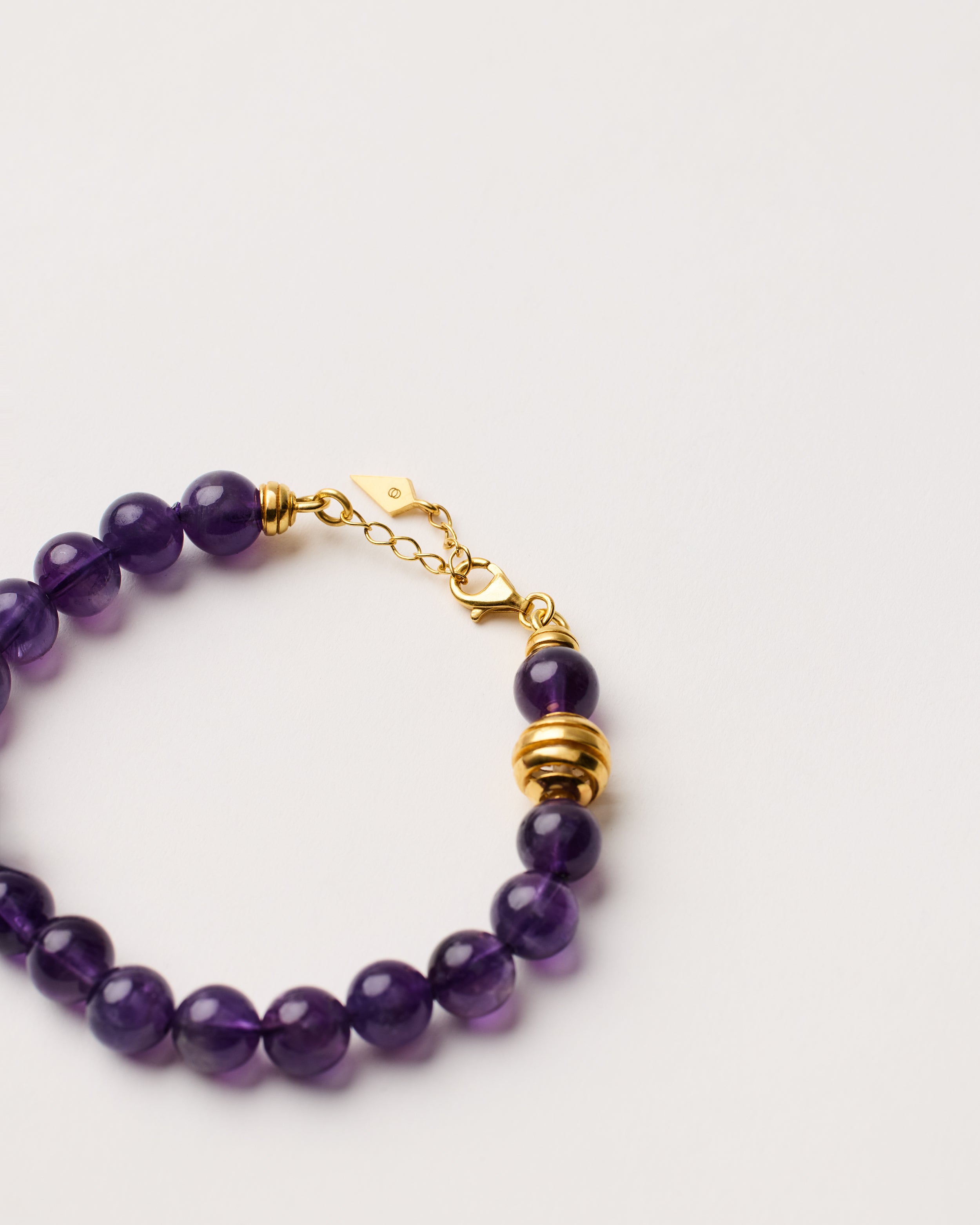 ETERNA VÉLA Amethyst bracelet with polished gold-plated silver spiral bead, 4 cm extension chain and clasp, arrowhead-shaped fantasy signature, and 8 mm faceted amethyst bead strand.