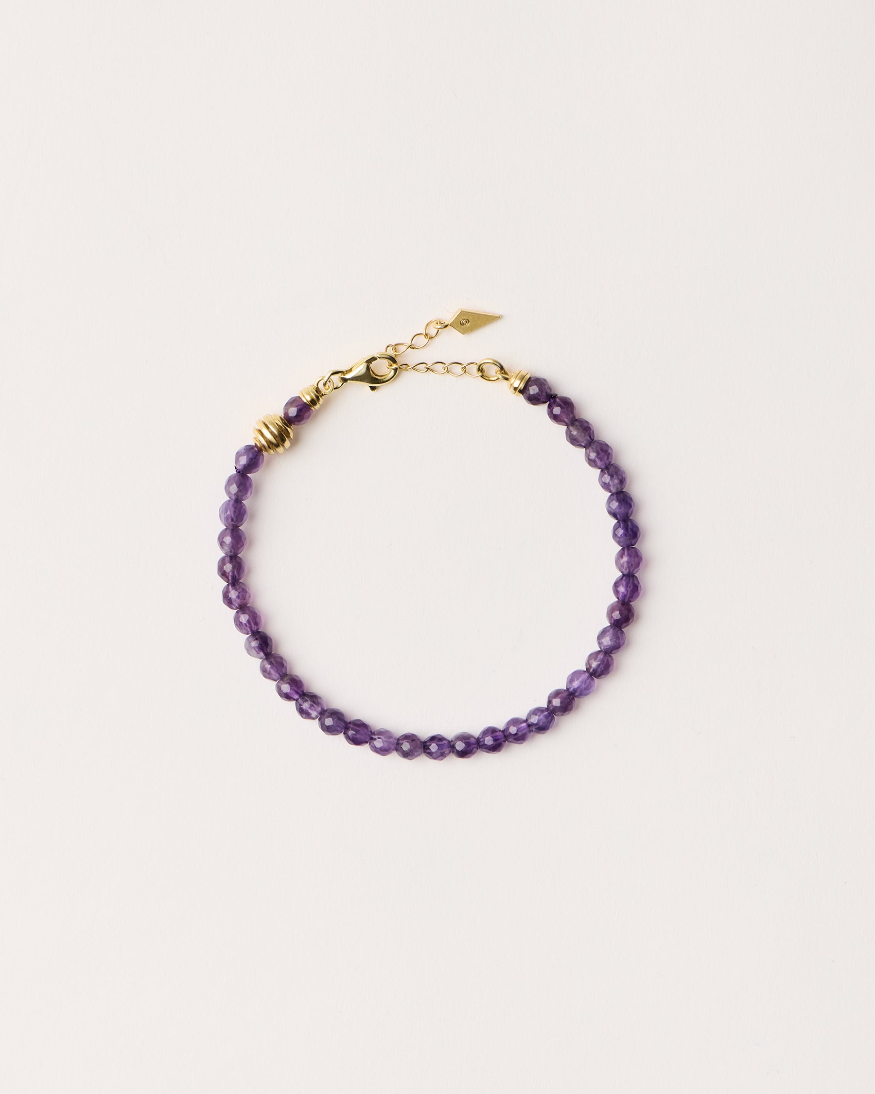 ETERNA VÉLA Amethyst bracelet with polished gold spiral bead, 4 cm extension chain and clasp, arrowhead-shaped fantasy signature, and 4 mm faceted amethyst bead strand.