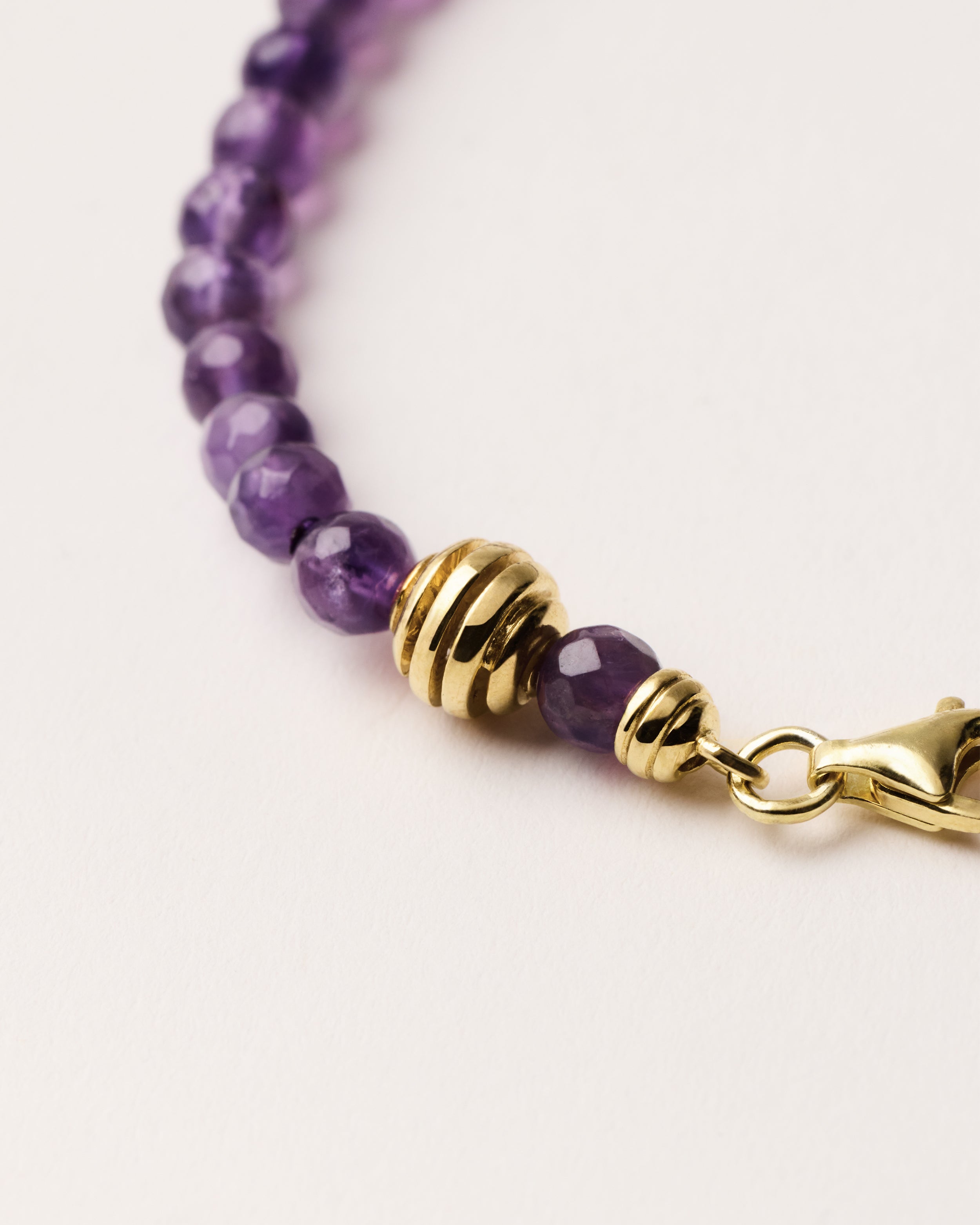 ETERNA VÉLA Amethyst bracelet with polished gold spiral bead, 4 cm extension chain and clasp, arrowhead-shaped fantasy signature, and 4 mm faceted amethyst bead strand.
