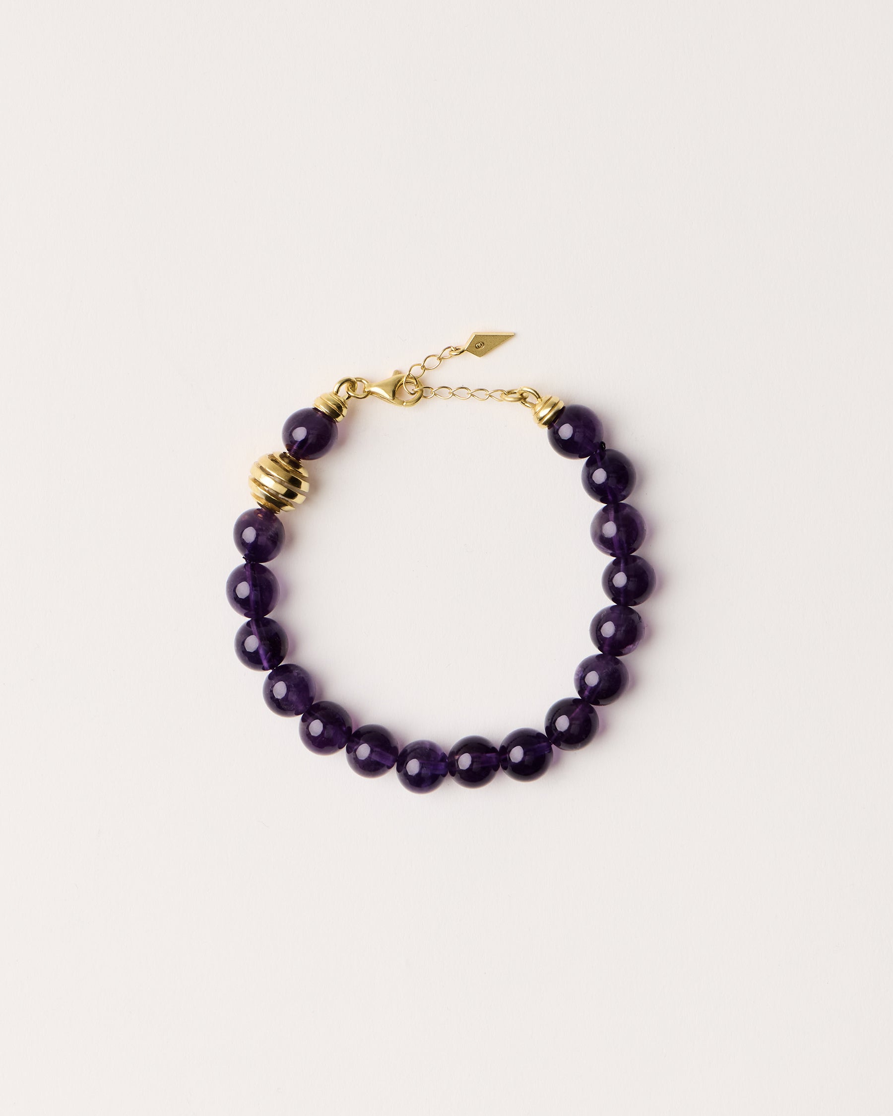 ETERNA VÉLA Amethyst bracelet with polished gold spiral bead, 4 cm extension chain and clasp, arrowhead-shaped fantasy signature, and 8 mm faceted amethyst bead strand.