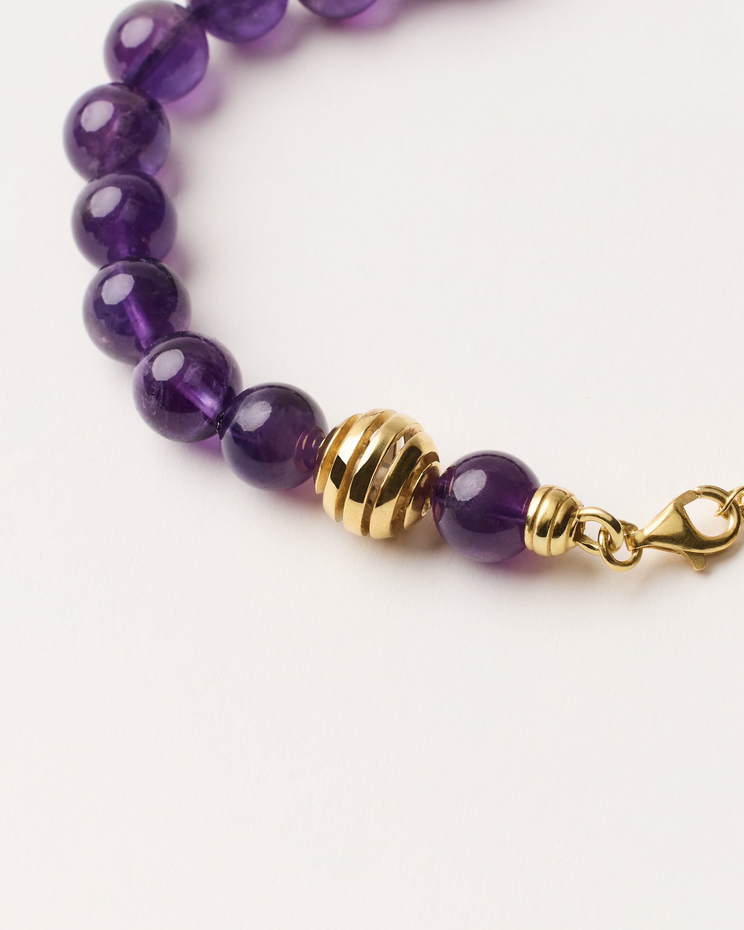ETERNA VÉLA Amethyst bracelet with polished gold spiral bead, 4 cm extension chain and clasp, arrowhead-shaped fantasy signature, and 8 mm faceted amethyst bead strand.