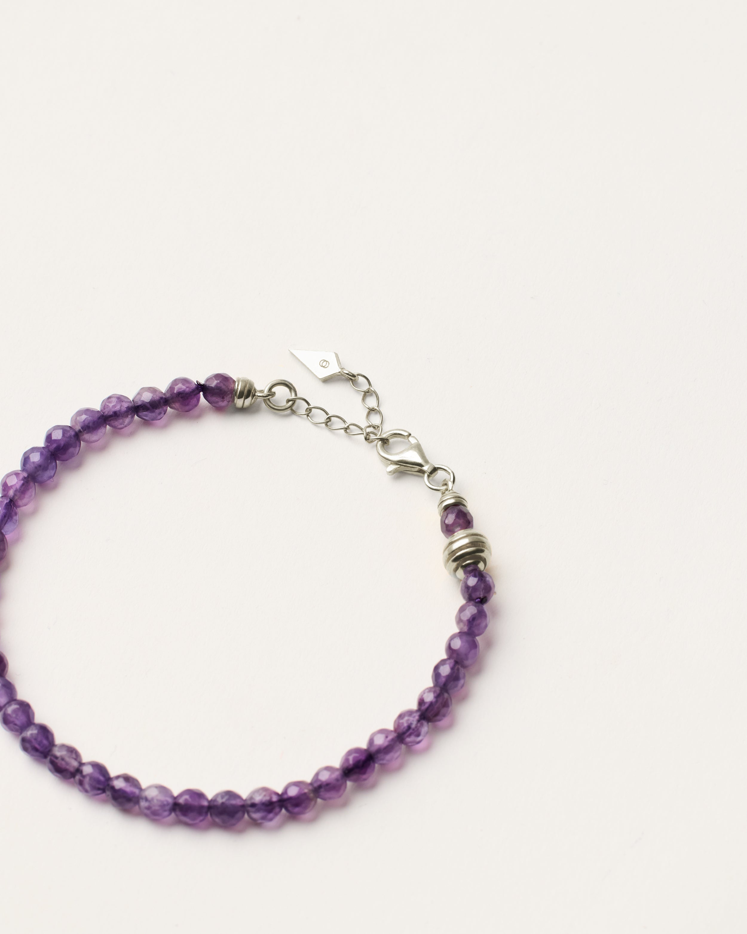 ETERNA VÉLA Amethyst bracelet with polished silver spiral bead, 4 cm extension chain and clasp, arrowhead-shaped fantasy signature, and 4 mm faceted amethyst bead strand.