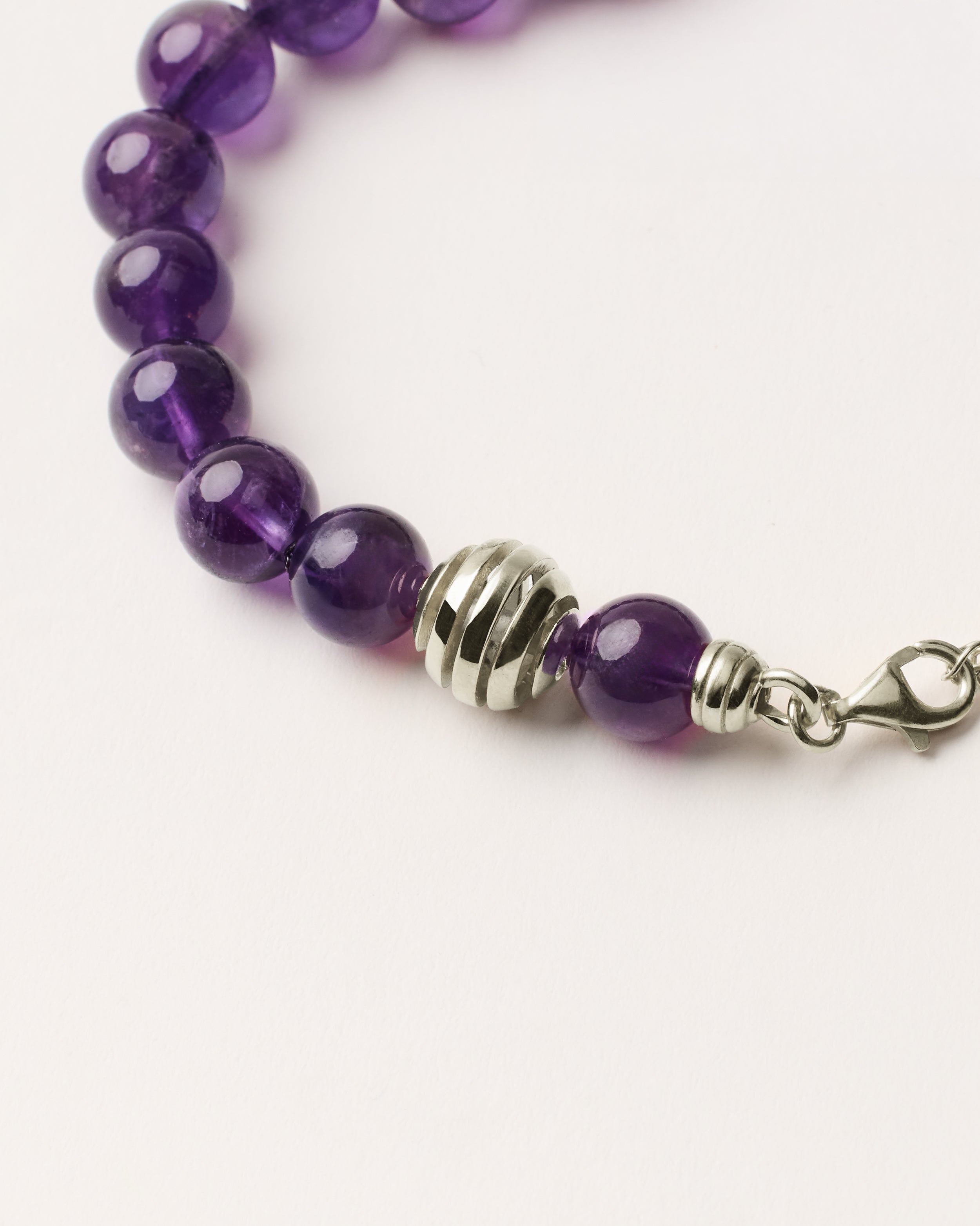 ETERNA VÉLA Amethyst bracelet with polished silver spiral bead, 4 cm extension chain and clasp, arrowhead-shaped fantasy signature, and 8 mm faceted amethyst bead strand.