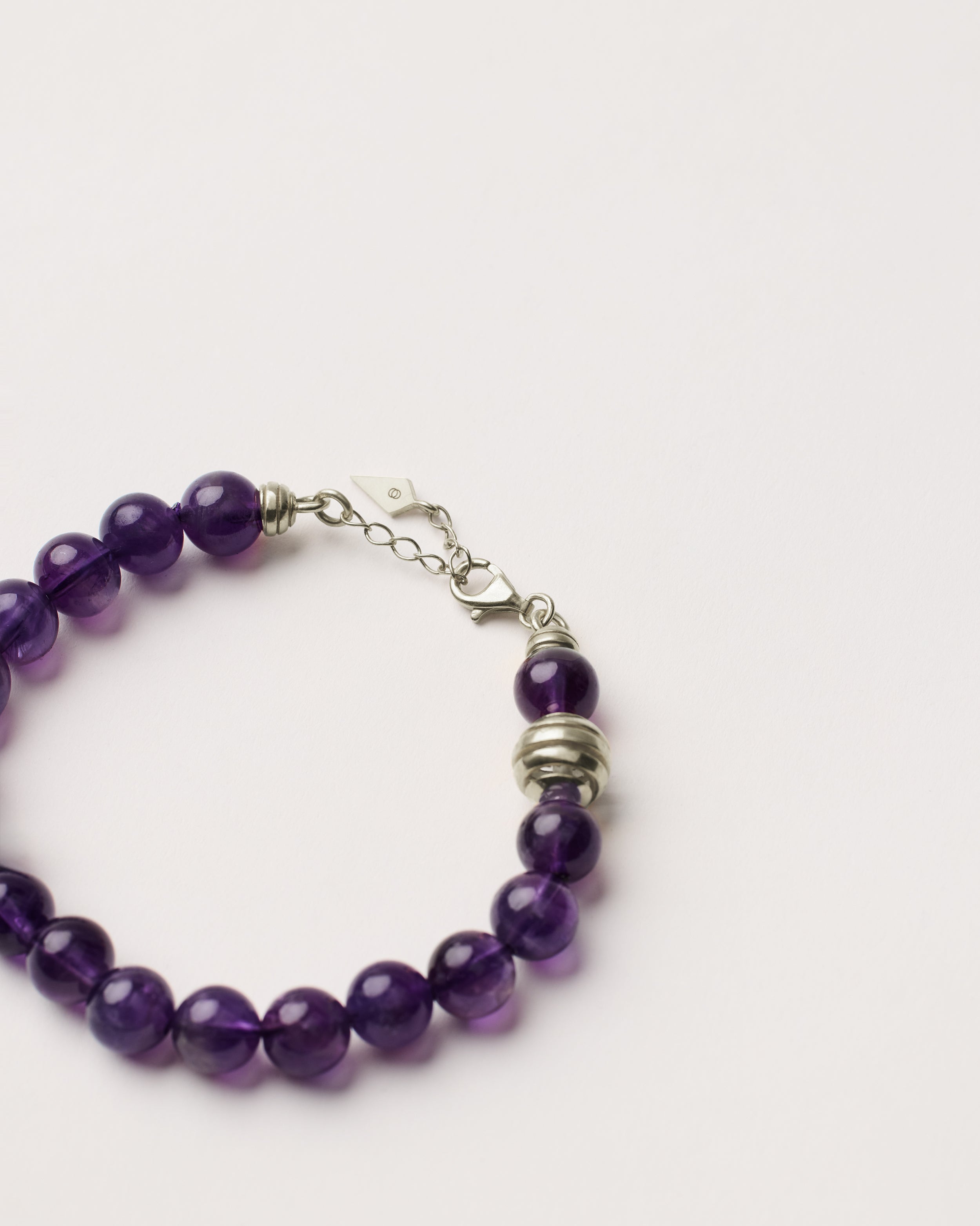 ETERNA VÉLA Amethyst bracelet with polished silver spiral bead, 4 cm extension chain and clasp, arrowhead-shaped fantasy signature, and 8 mm faceted amethyst bead strand.