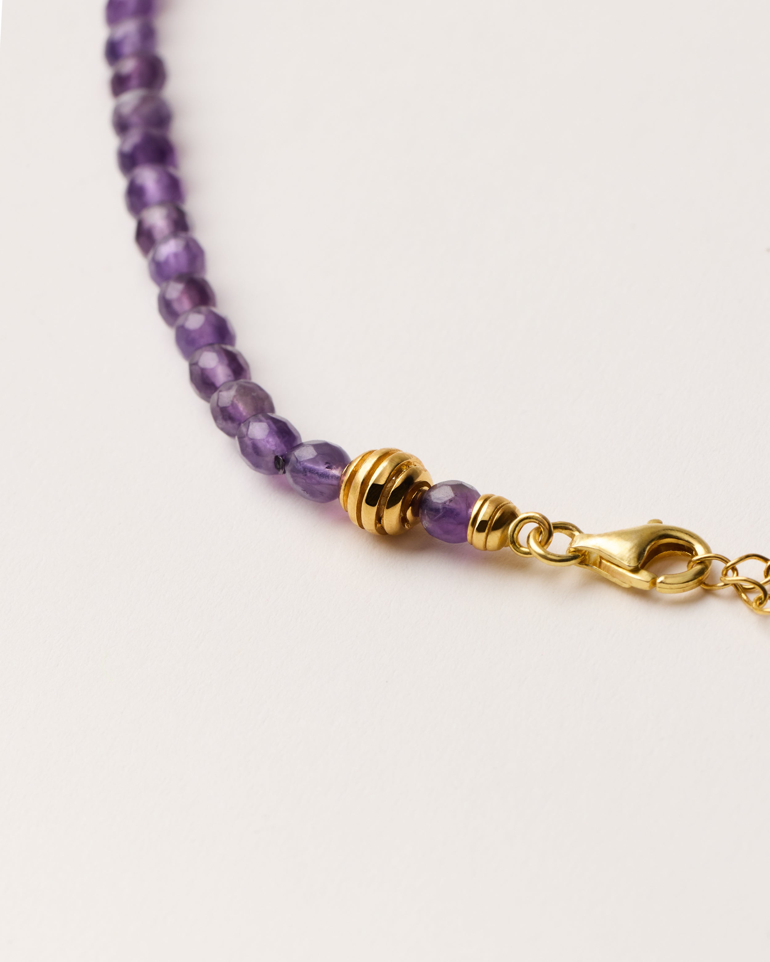 ETERNA VÉLA Amethyst necklace with polished gold-plated silver spiral bead, 8 cm extension chain and clasp, arrowhead-shaped fantasy signature, and 4 mm faceted amethyst bead strand.