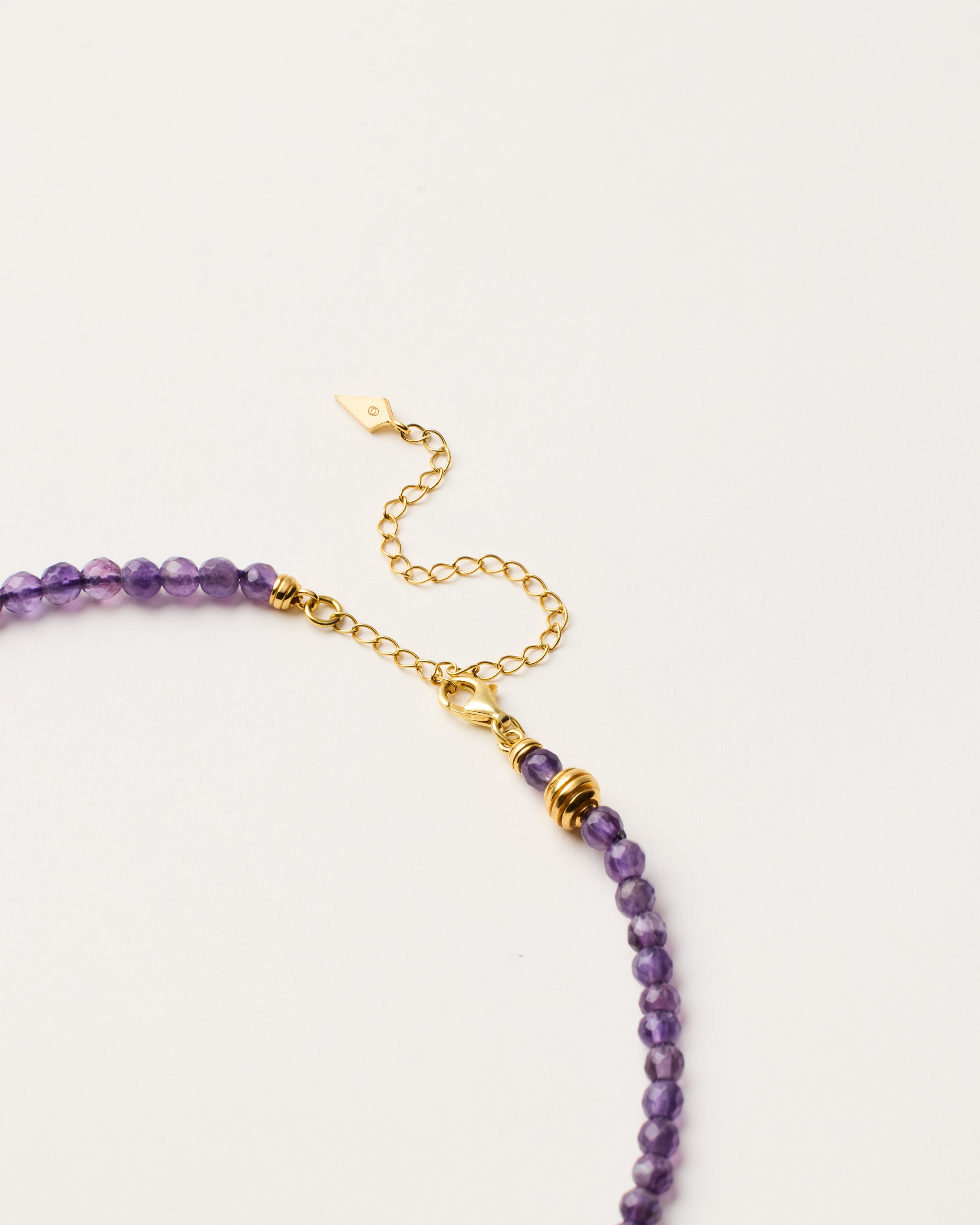 ETERNA VÉLA Amethyst necklace with polished gold-plated silver spiral bead, 8 cm extension chain and clasp, arrowhead-shaped fantasy signature, and 4 mm faceted amethyst bead strand.
