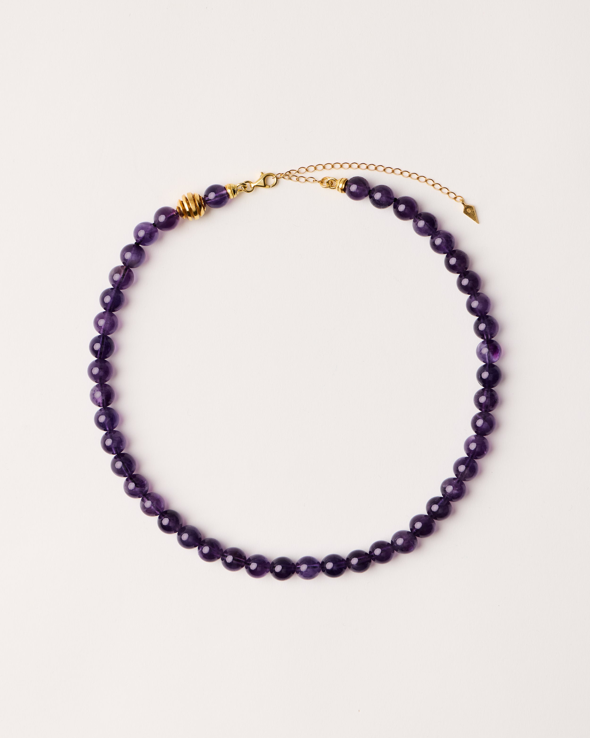 ETERNA VÉLA Amethyst necklace with polished gold-plated silver spiral bead, 8 cm extension chain and clasp, arrowhead-shaped fantasy signature, and 8 mm faceted amethyst bead strand.