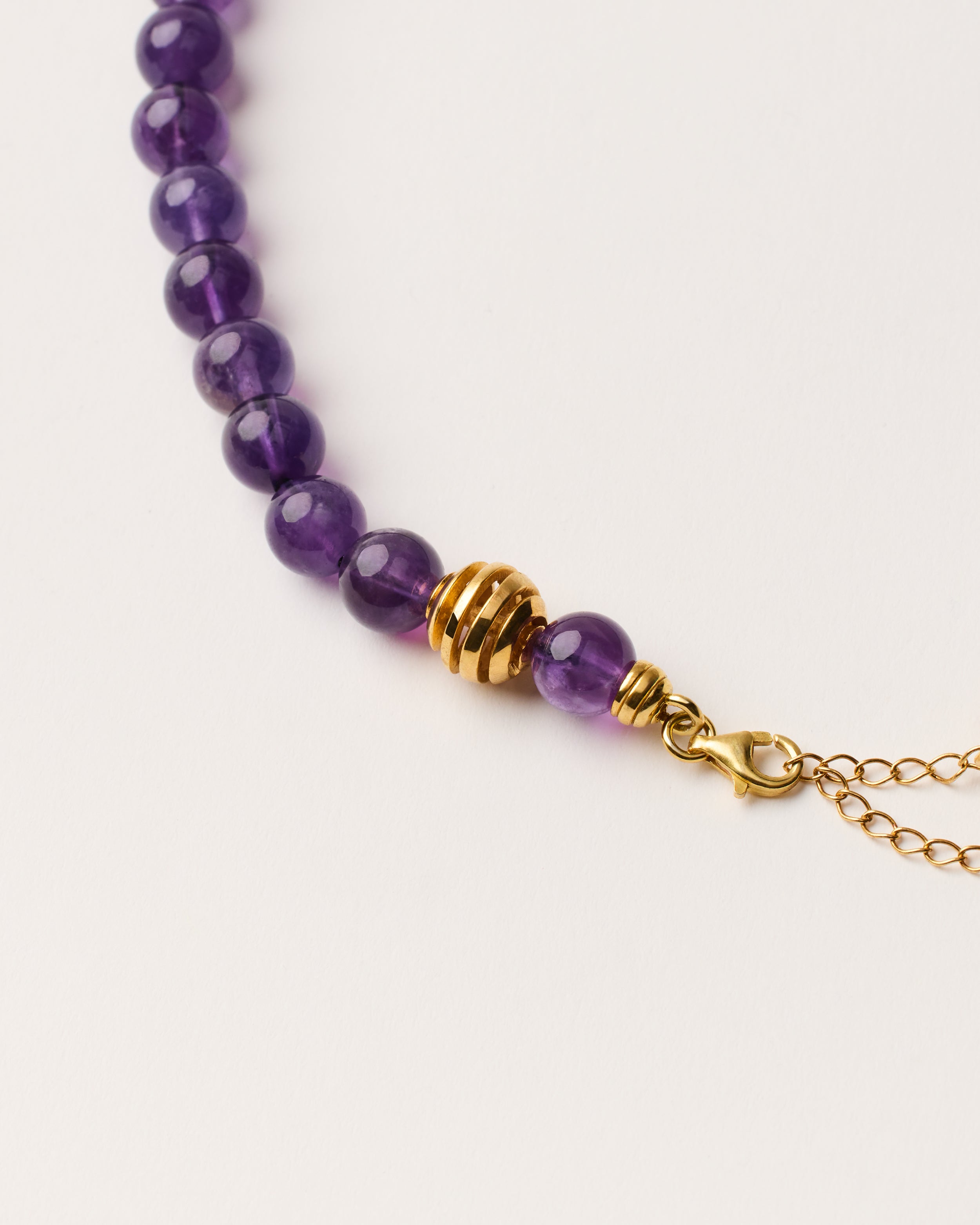 ETERNA VÉLA Amethyst necklace with polished gold-plated silver spiral bead, 8 cm extension chain and clasp, arrowhead-shaped fantasy signature, and 8 mm faceted amethyst bead strand.