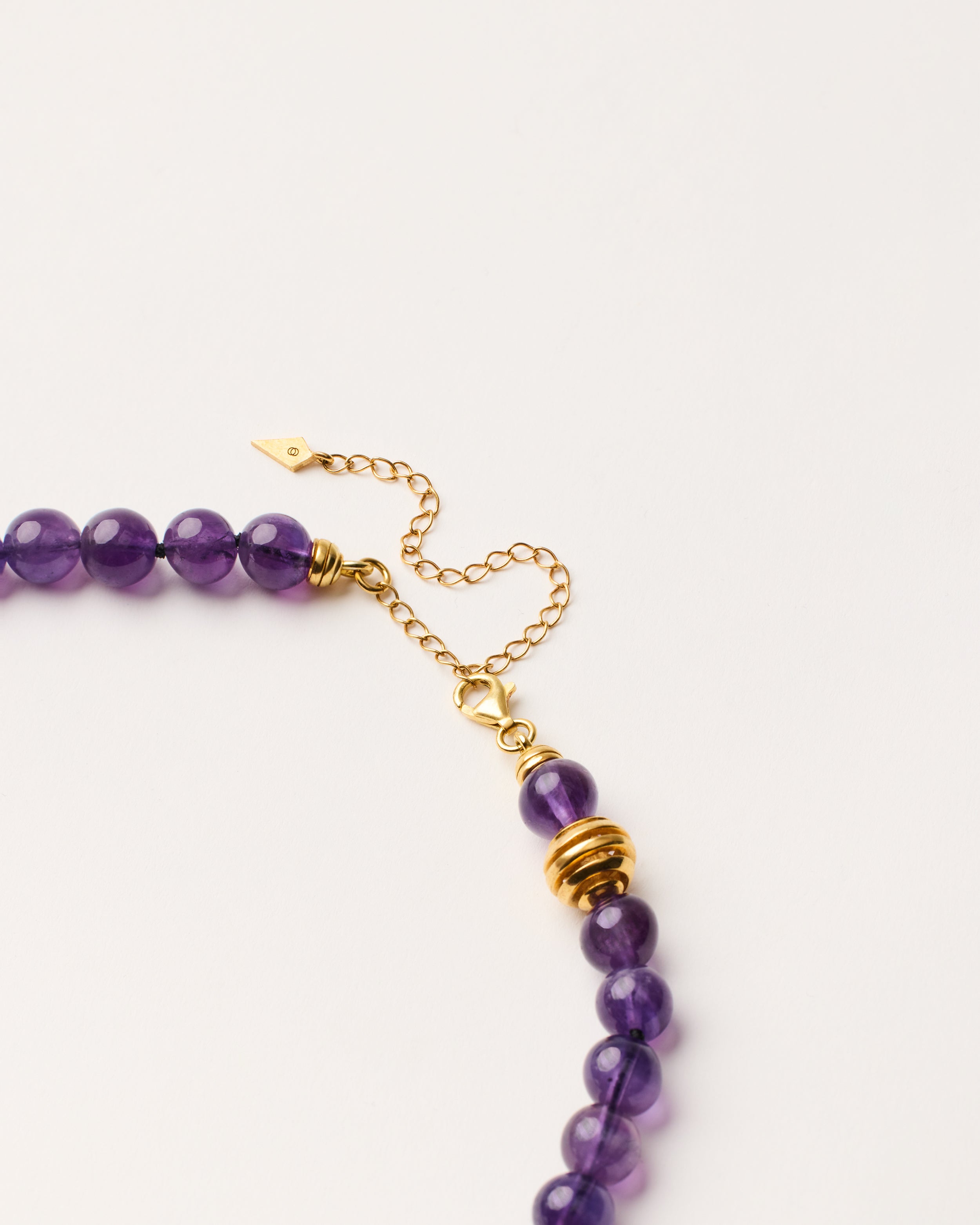 ETERNA VÉLA Amethyst necklace with polished gold-plated silver spiral bead, 8 cm extension chain and clasp, arrowhead-shaped fantasy signature, and 8 mm faceted amethyst bead strand.