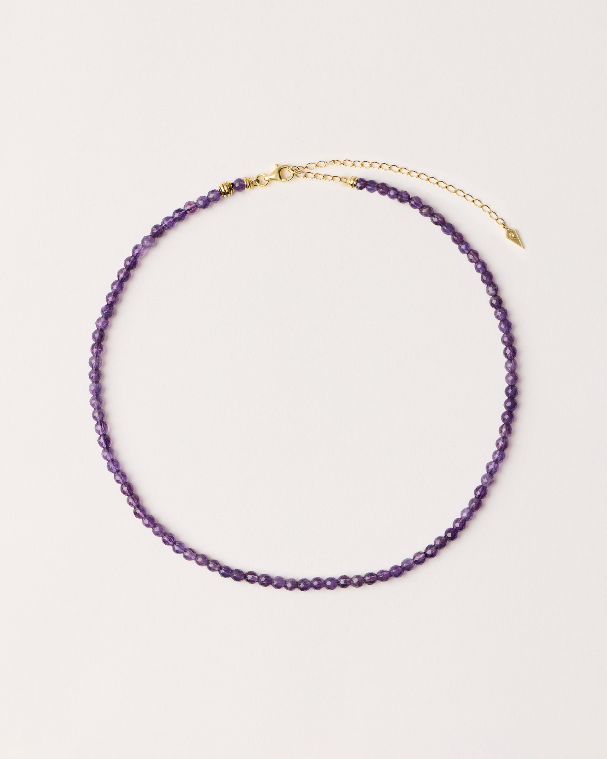 ETERNA VÉLA Amethyst necklace with polished gold spiral bead, 8 cm extension chain and clasp, arrowhead-shaped fantasy signature, and 4 mm faceted amethyst bead strand.