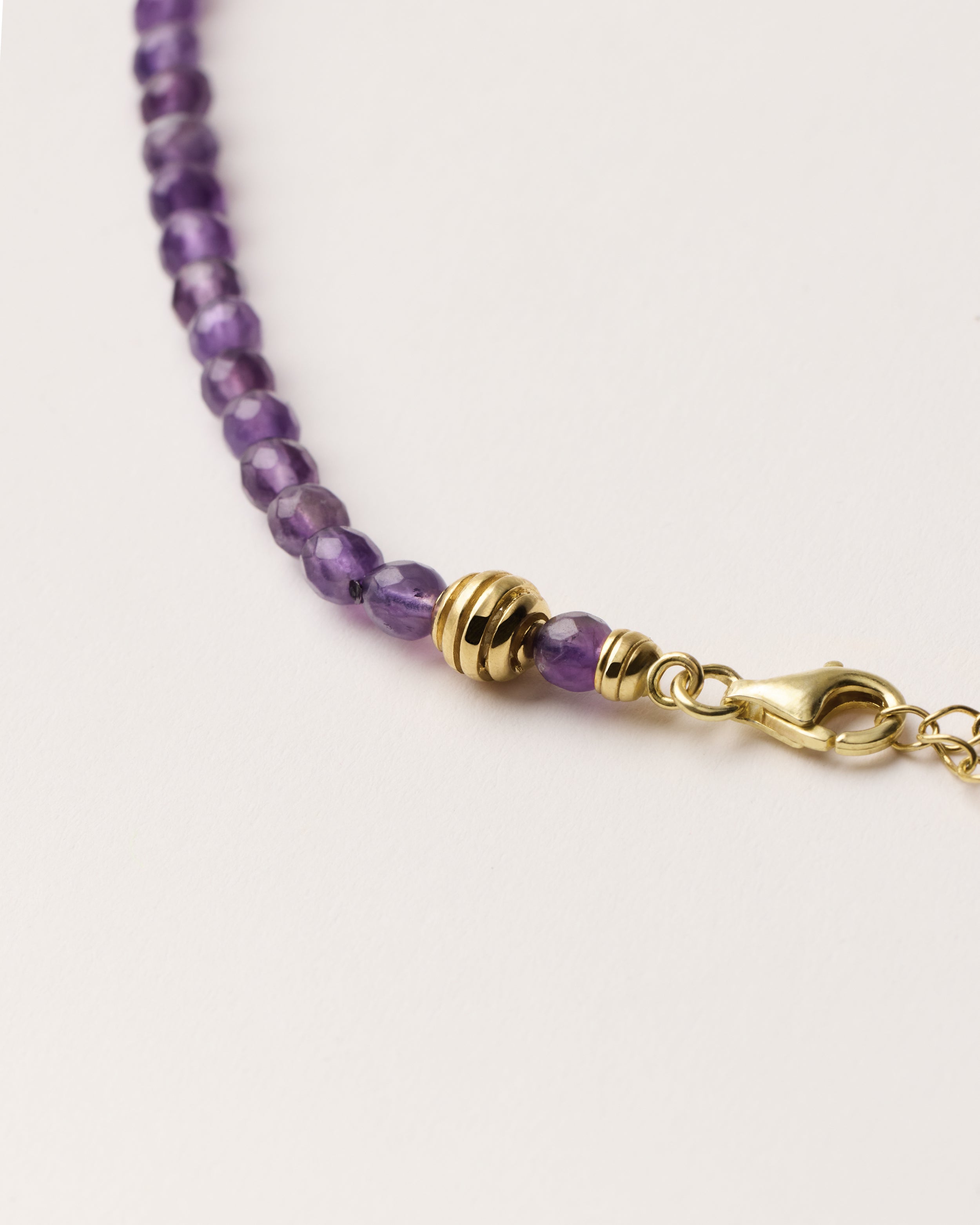 ETERNA VÉLA Amethyst necklace with polished gold spiral bead, 8 cm extension chain and clasp, arrowhead-shaped fantasy signature, and 4 mm faceted amethyst bead strand.