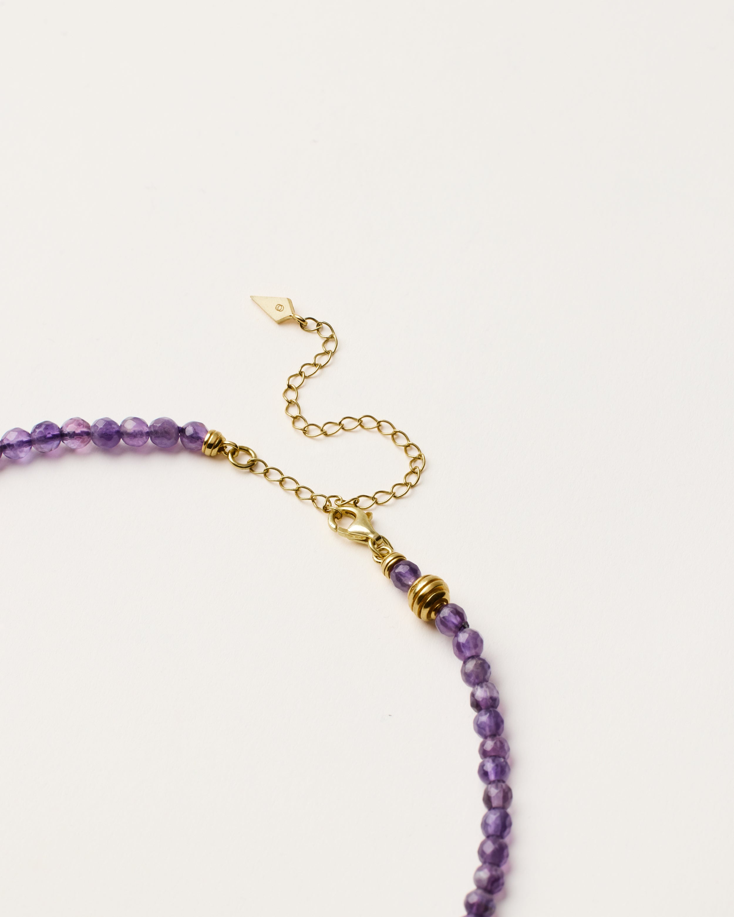 ETERNA VÉLA Amethyst necklace with polished gold spiral bead, 8 cm extension chain and clasp, arrowhead-shaped fantasy signature, and 4 mm faceted amethyst bead strand.