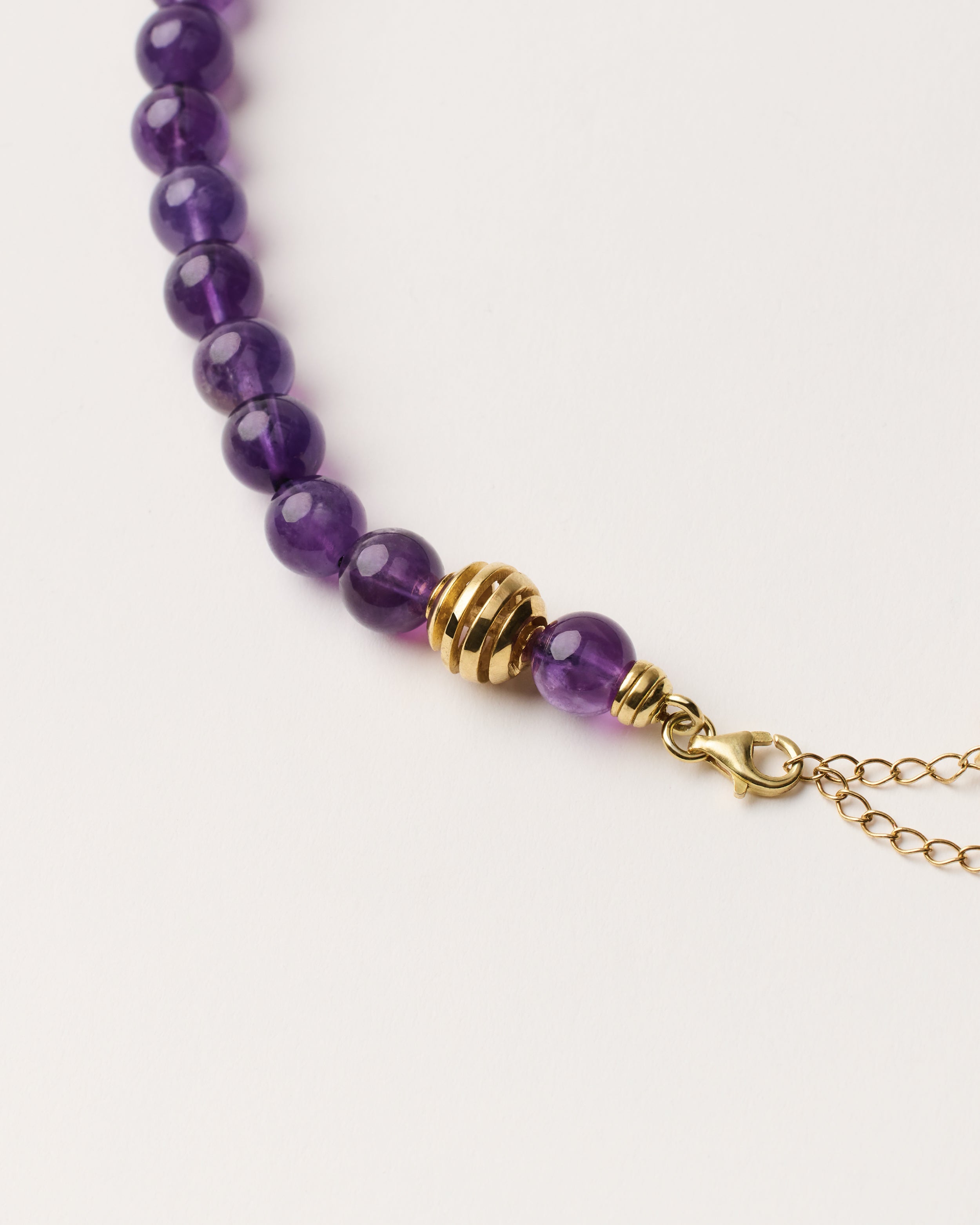 ETERNA VÉLA Amethyst necklace with polished gold spiral bead, 8 cm extension chain and clasp, arrowhead-shaped fantasy signature, and 8 mm faceted amethyst bead strand.