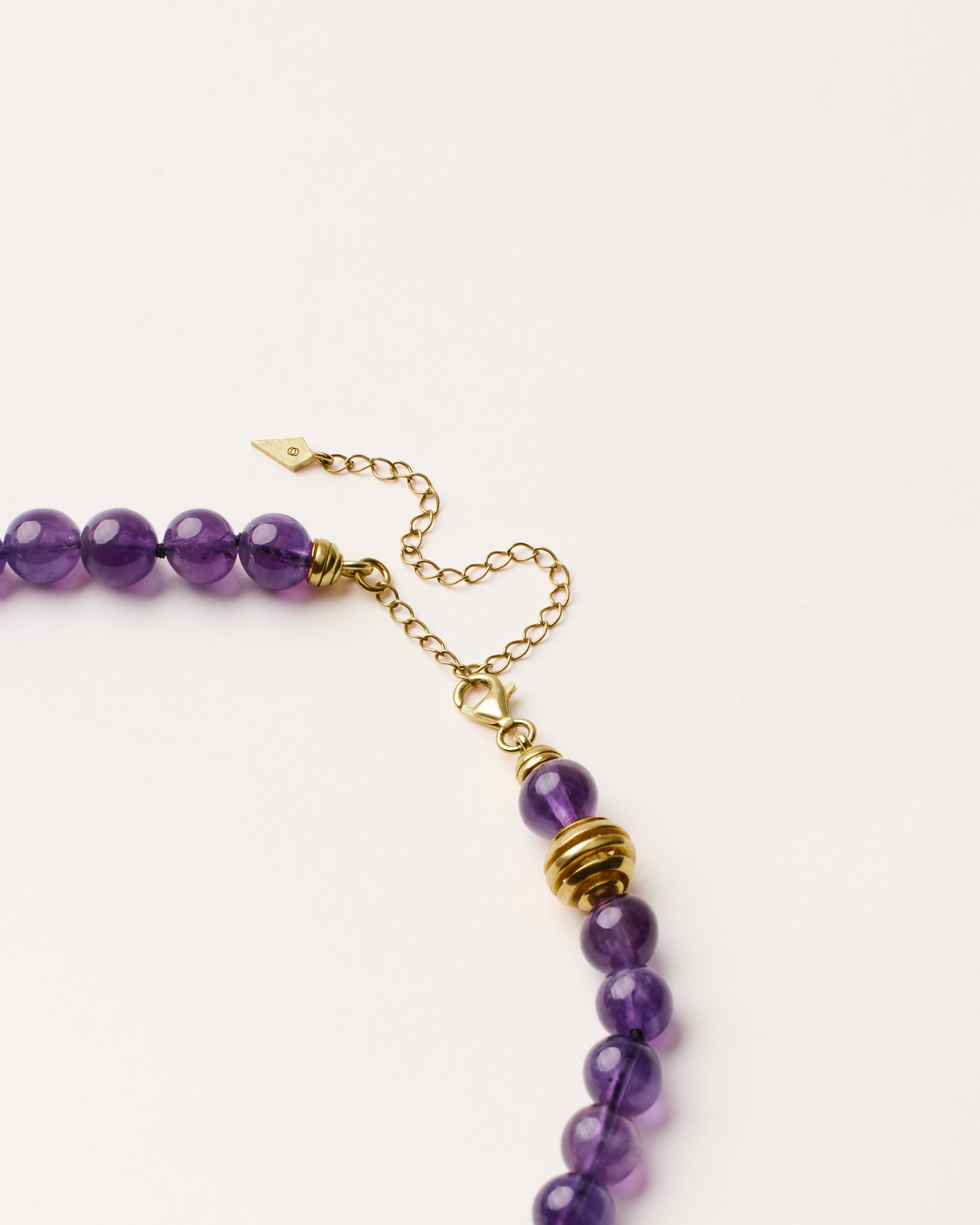 ETERNA VÉLA Amethyst necklace with polished gold spiral bead, 8 cm extension chain and clasp, arrowhead-shaped fantasy signature, and 8 mm faceted amethyst bead strand.