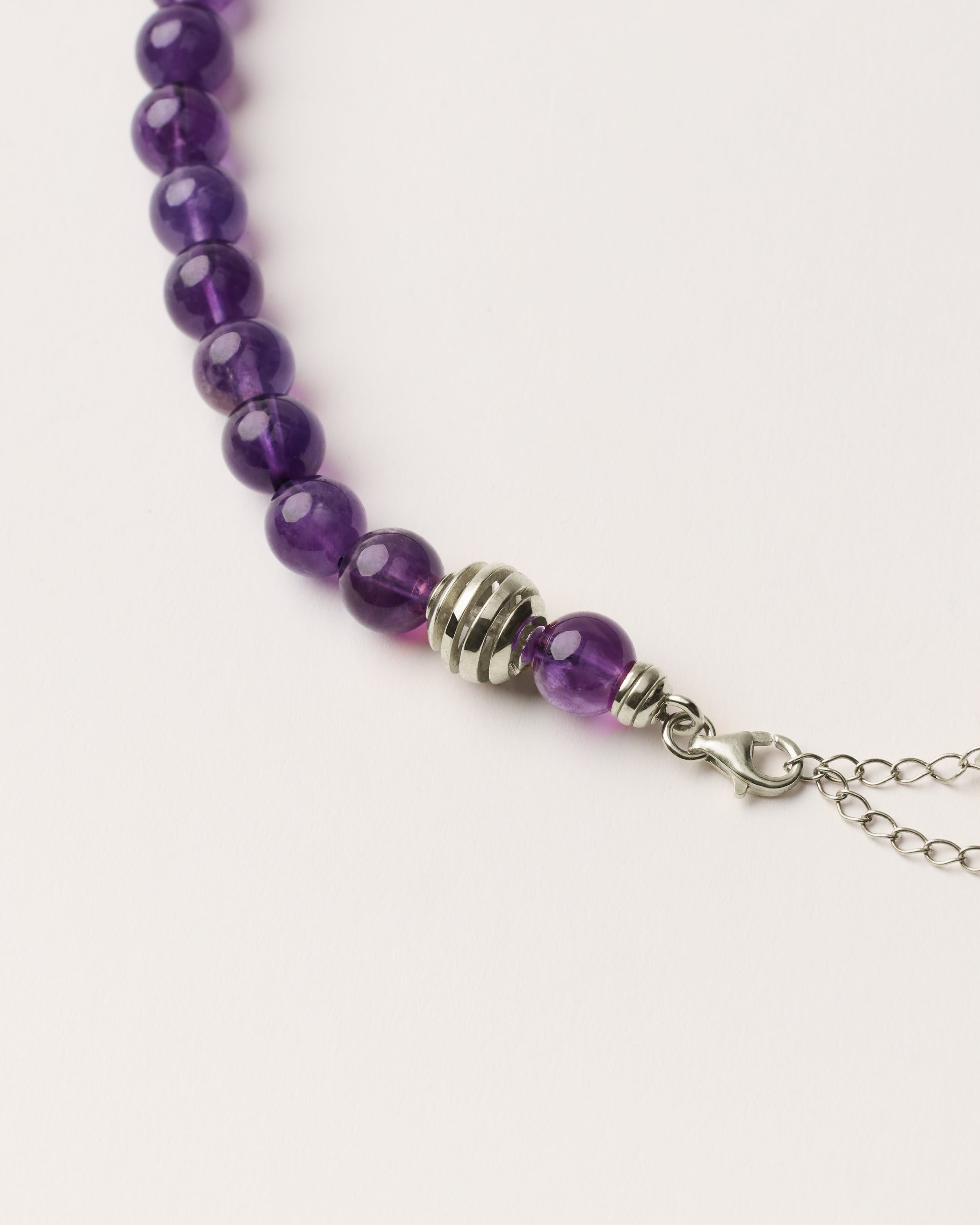 ETERNA VÉLA Amethyst necklace with polished silver spiral bead, 8 cm extension chain and clasp, arrowhead-shaped fantasy signature, and 8 mm faceted amethyst bead strand.