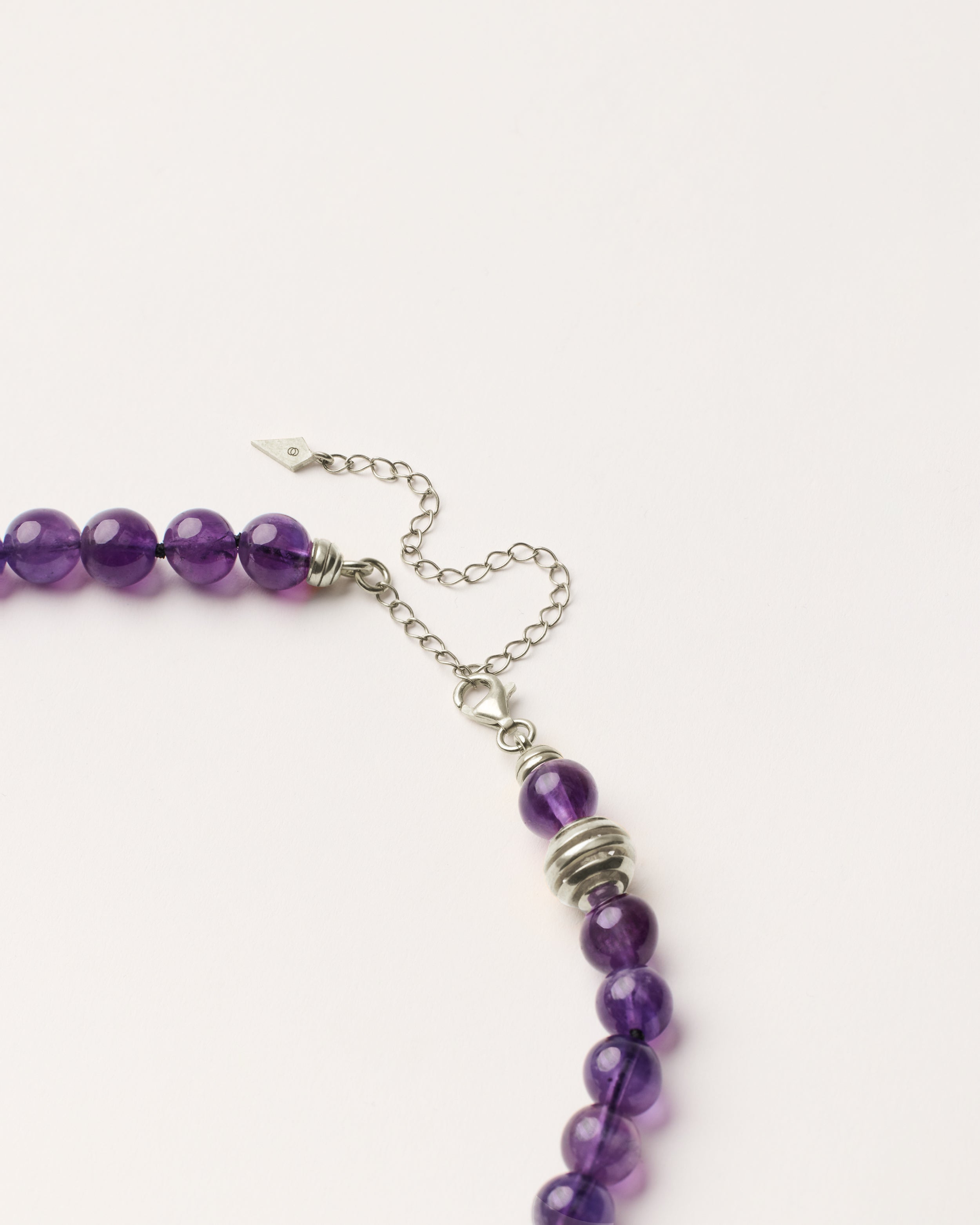 ETERNA VÉLA Amethyst necklace with polished silver spiral bead, 8 cm extension chain and clasp, arrowhead-shaped fantasy signature, and 8 mm faceted amethyst bead strand.