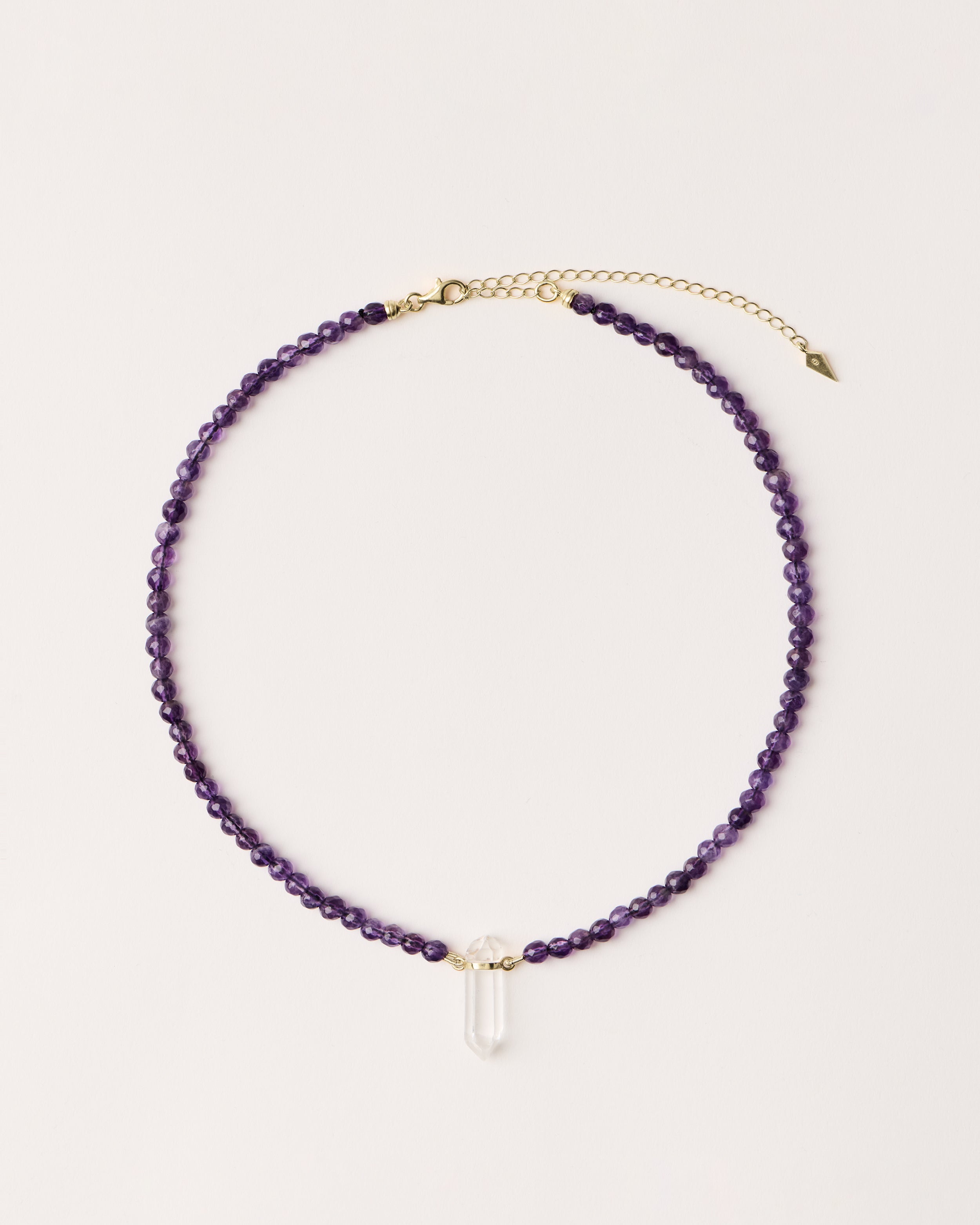 ENCARA VÉLA Amethyst necklace with raw polished quartz point pendant, gold 8 cm extension chain and clasp, arrowhead-shaped fantasy signature, and 4 mm faceted amethyst bead strand.