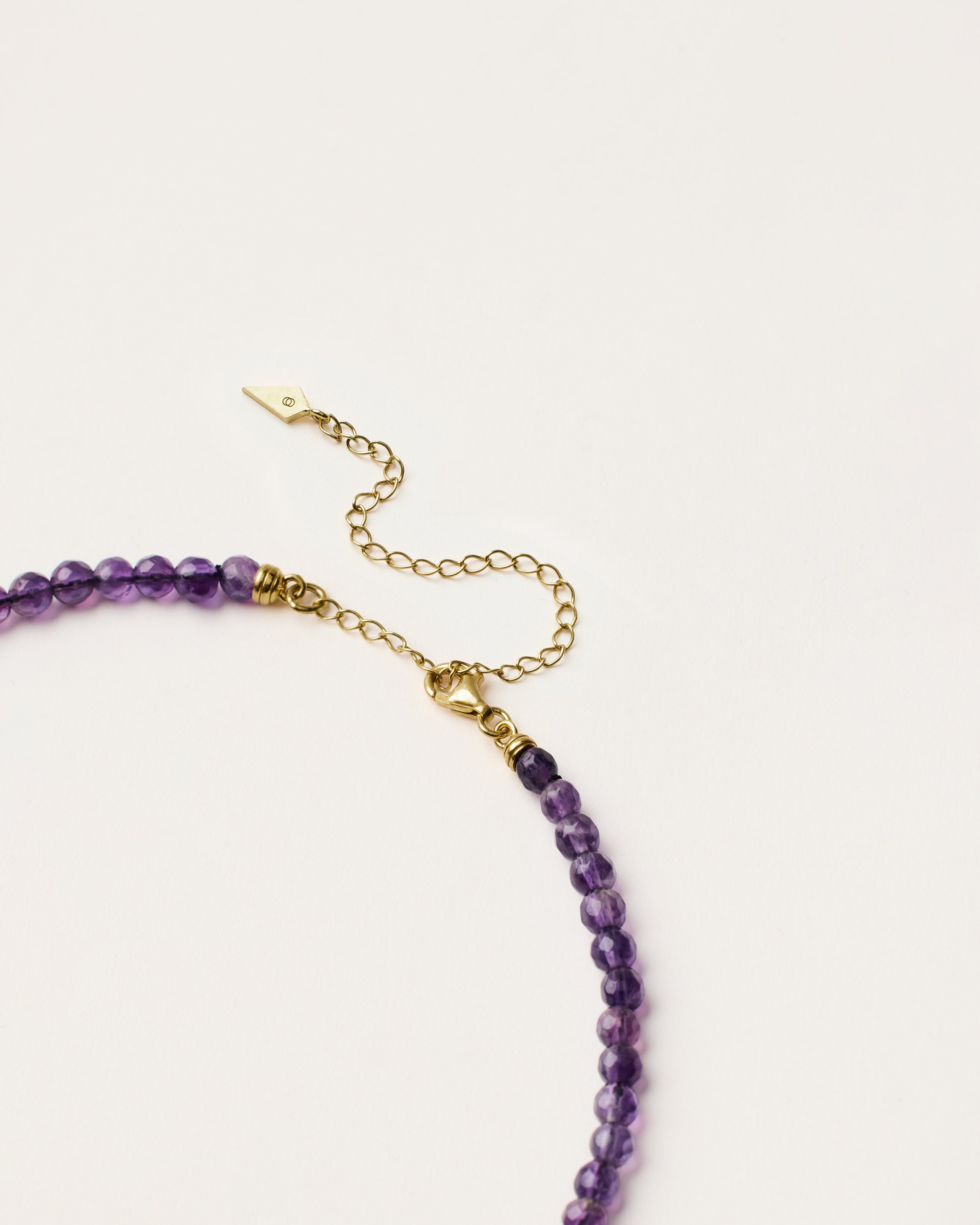 ENCARA VÉLA Amethyst necklace with raw polished quartz point pendant, gold 8 cm extension chain and clasp, arrowhead-shaped fantasy signature, and 4 mm faceted amethyst bead strand.