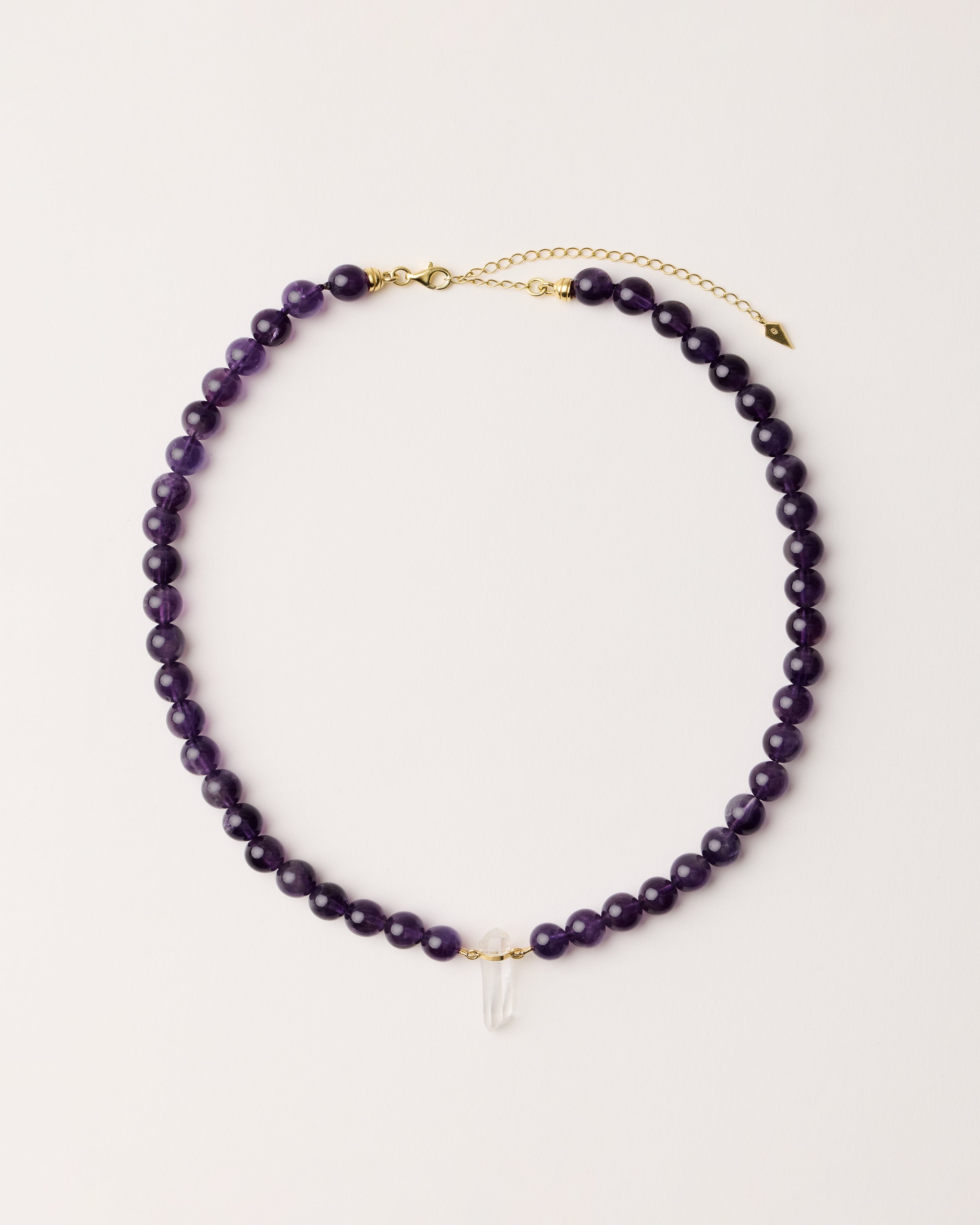 ENCARA VÉLA Amethyst necklace with raw polished quartz point pendant, gold 8 cm extension chain and clasp, arrowhead-shaped fantasy signature, and 8 mm faceted amethyst bead strand.