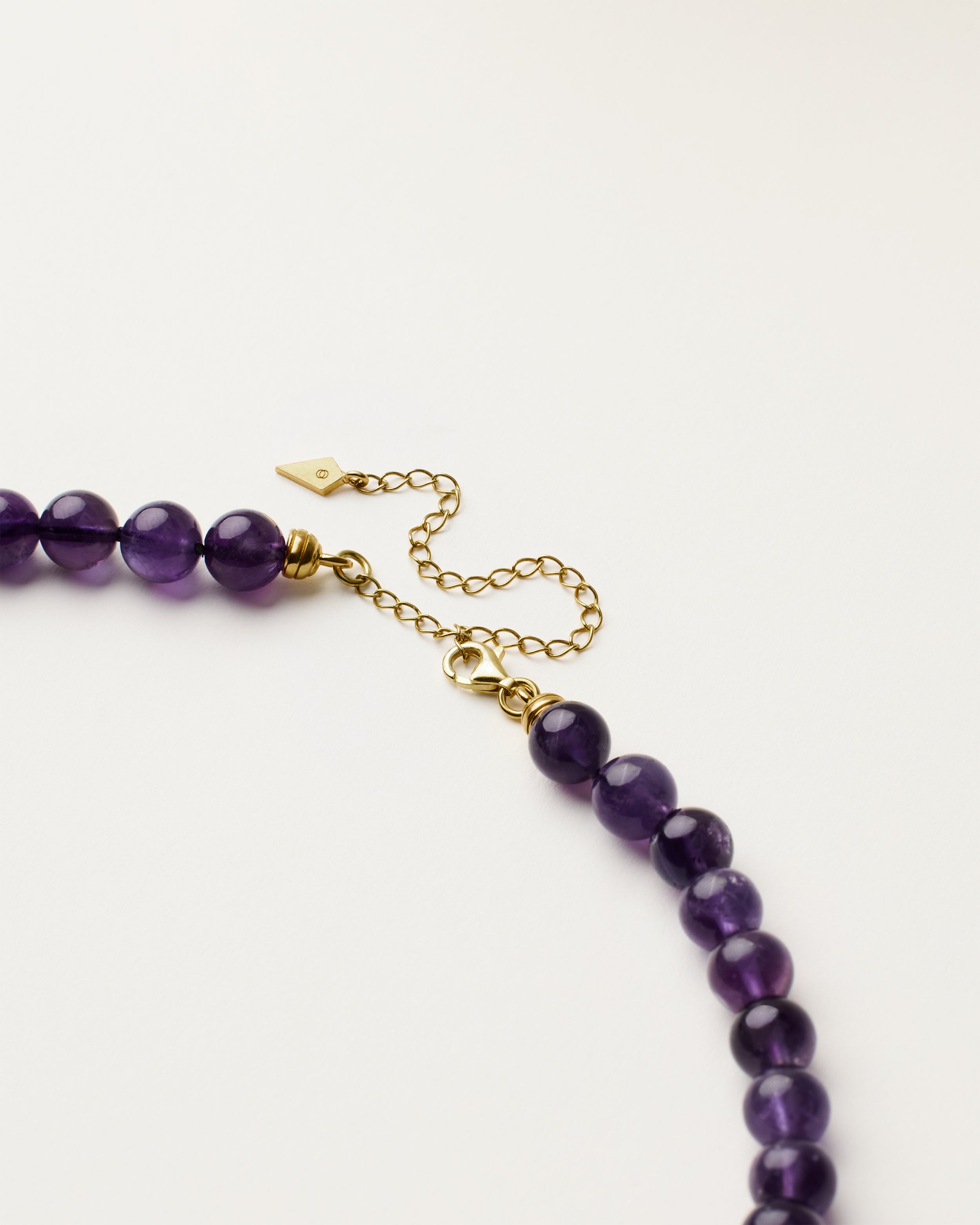 ENCARA VÉLA Amethyst necklace with raw polished quartz point pendant, gold 8 cm extension chain and clasp, arrowhead-shaped fantasy signature, and 8 mm faceted amethyst bead strand.