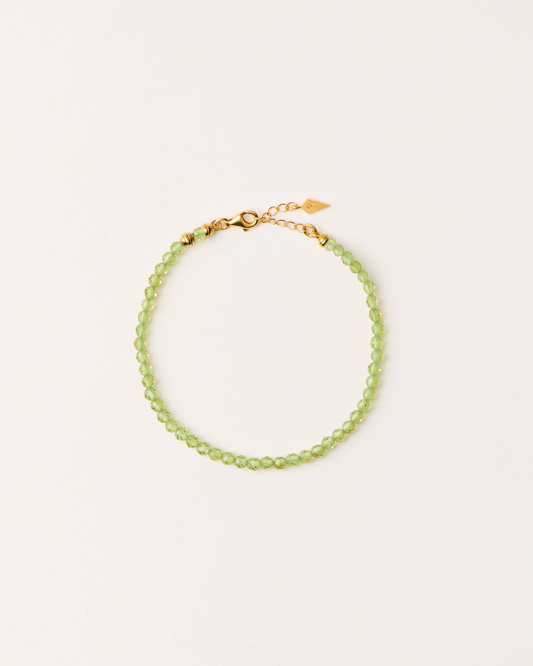 ETERNA OLMAR Peridot bracelet with polished gold-plated silver spiral bead, 4 cm extension chain and clasp, arrowhead-shaped fantasy signature, and 4 mm faceted chrysolite bead strand.