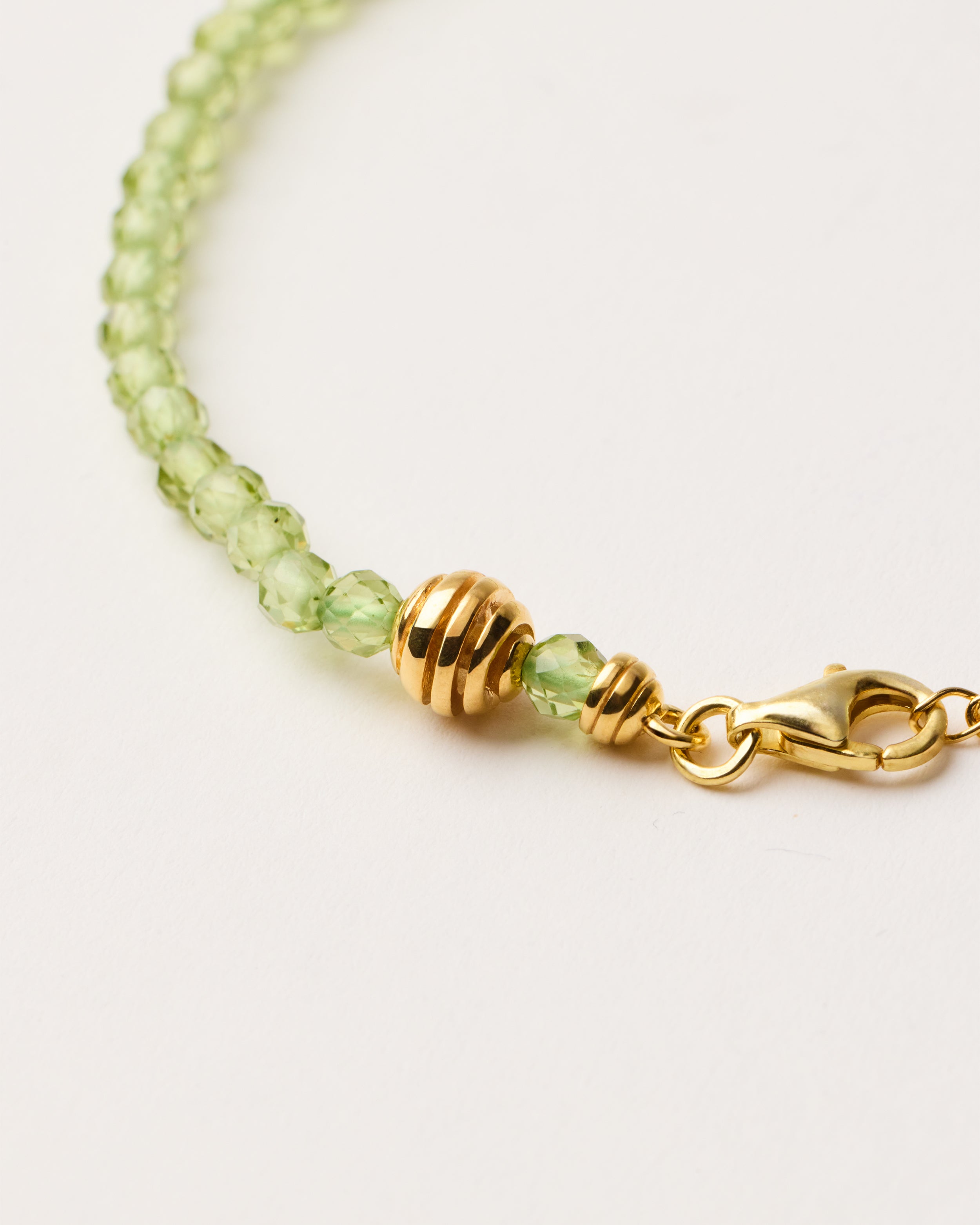 ETERNA OLMAR Peridot bracelet with polished gold-plated silver spiral bead, 4 cm extension chain and clasp, arrowhead-shaped fantasy signature, and 4 mm faceted chrysolite bead strand.