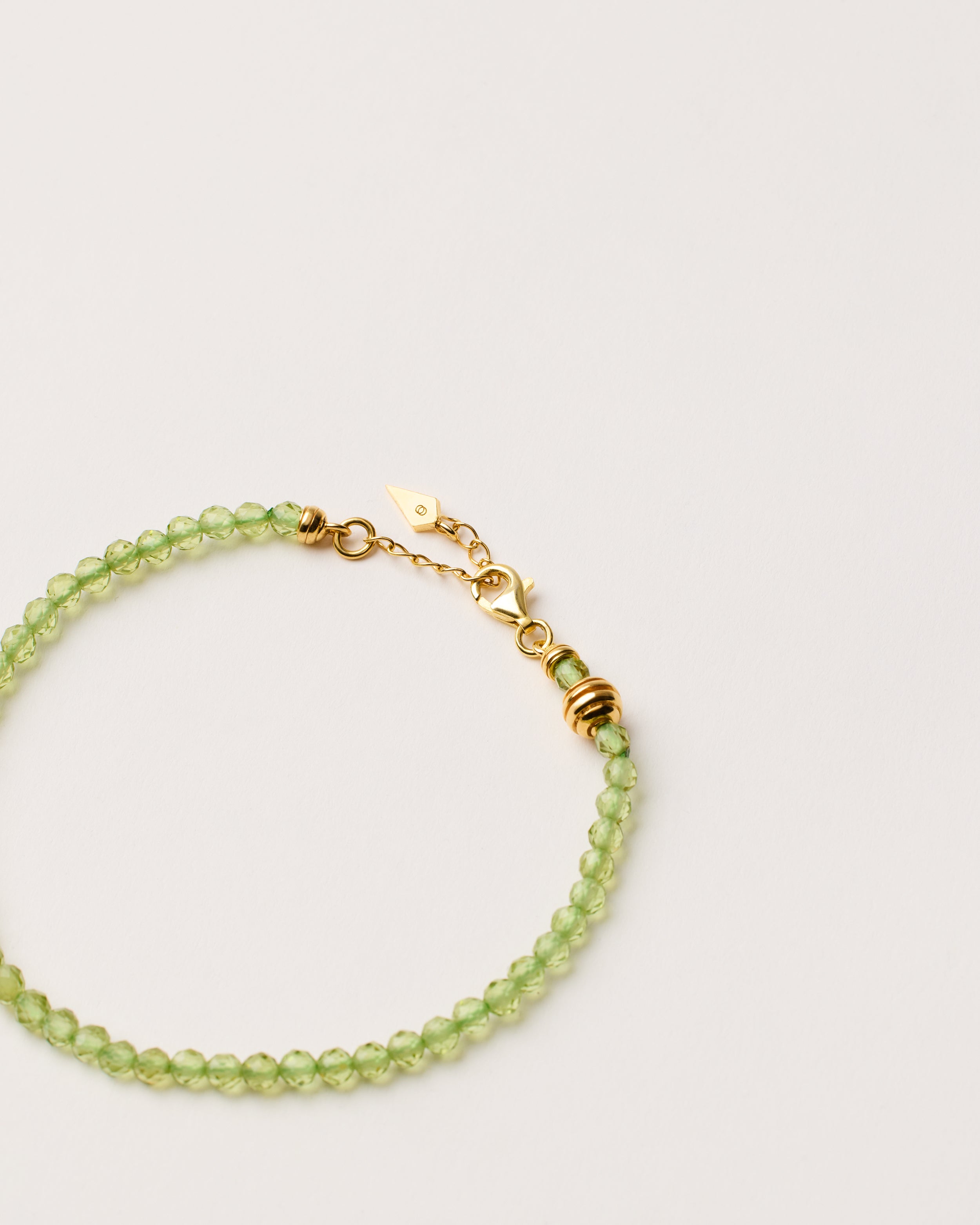 ETERNA OLMAR Peridot bracelet with polished gold-plated silver spiral bead, 4 cm extension chain and clasp, arrowhead-shaped fantasy signature, and 4 mm faceted chrysolite bead strand.