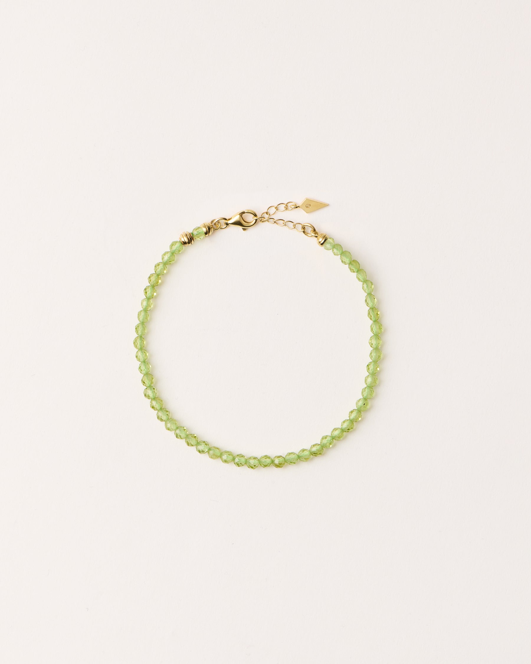 ETERNA OLMAR Peridot bracelet with polished gold spiral bead, 4 cm extension chain and clasp, arrowhead-shaped fantasy signature, and 4 mm faceted chrysolite bead strand.