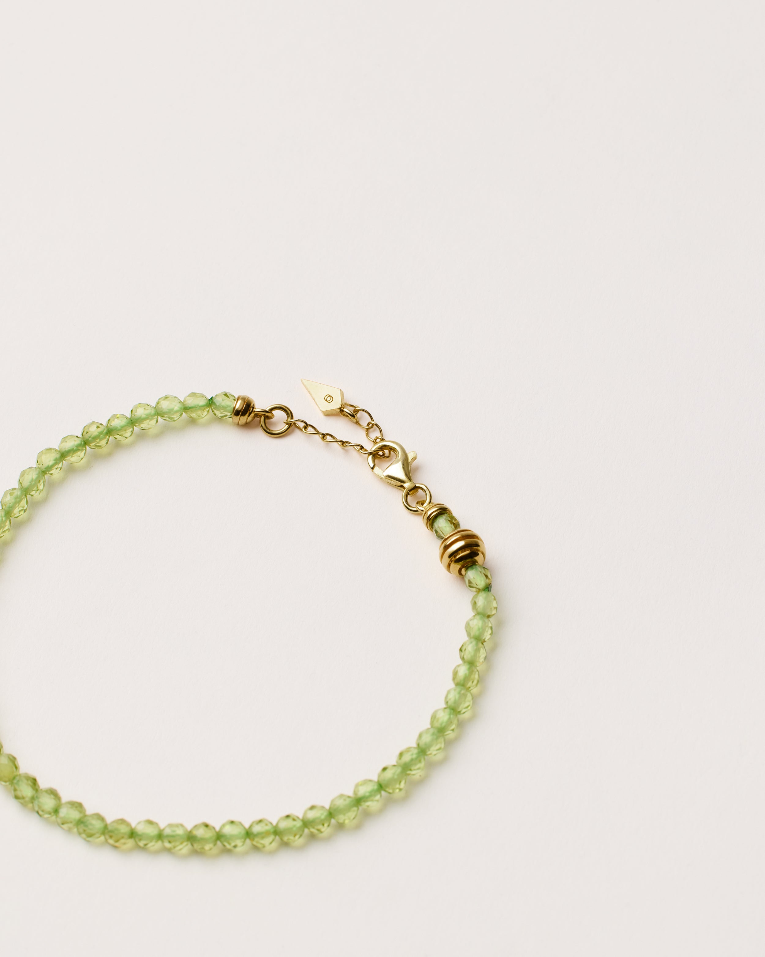 ETERNA OLMAR Peridot bracelet with polished gold spiral bead, 4 cm extension chain and clasp, arrowhead-shaped fantasy signature, and 4 mm faceted chrysolite bead strand.